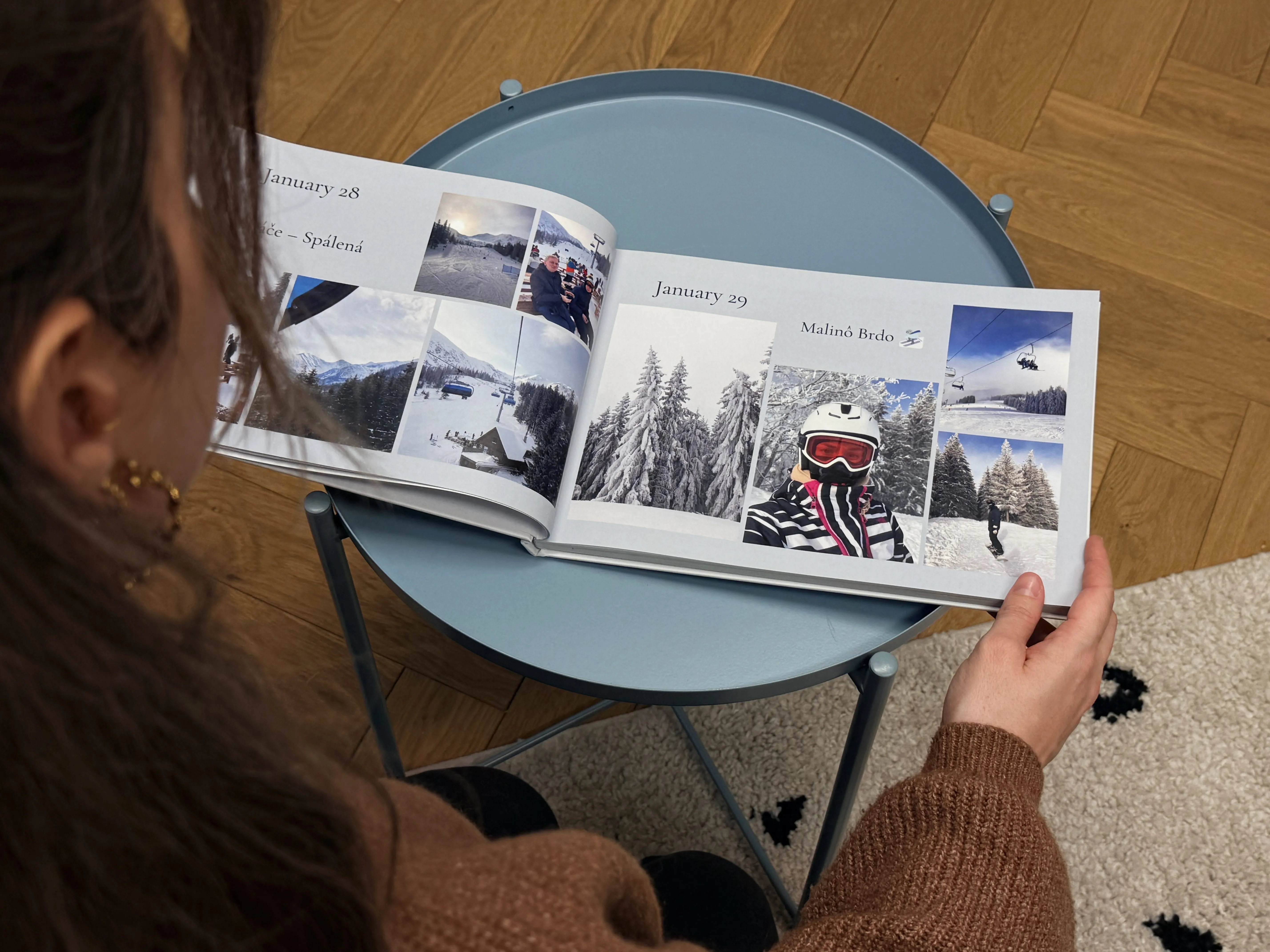Person, die ein offenes Fotobuch auf einem blauen Tisch betrachtet, mit Schneelandschaften und Bildern zum Thema Skifahren.