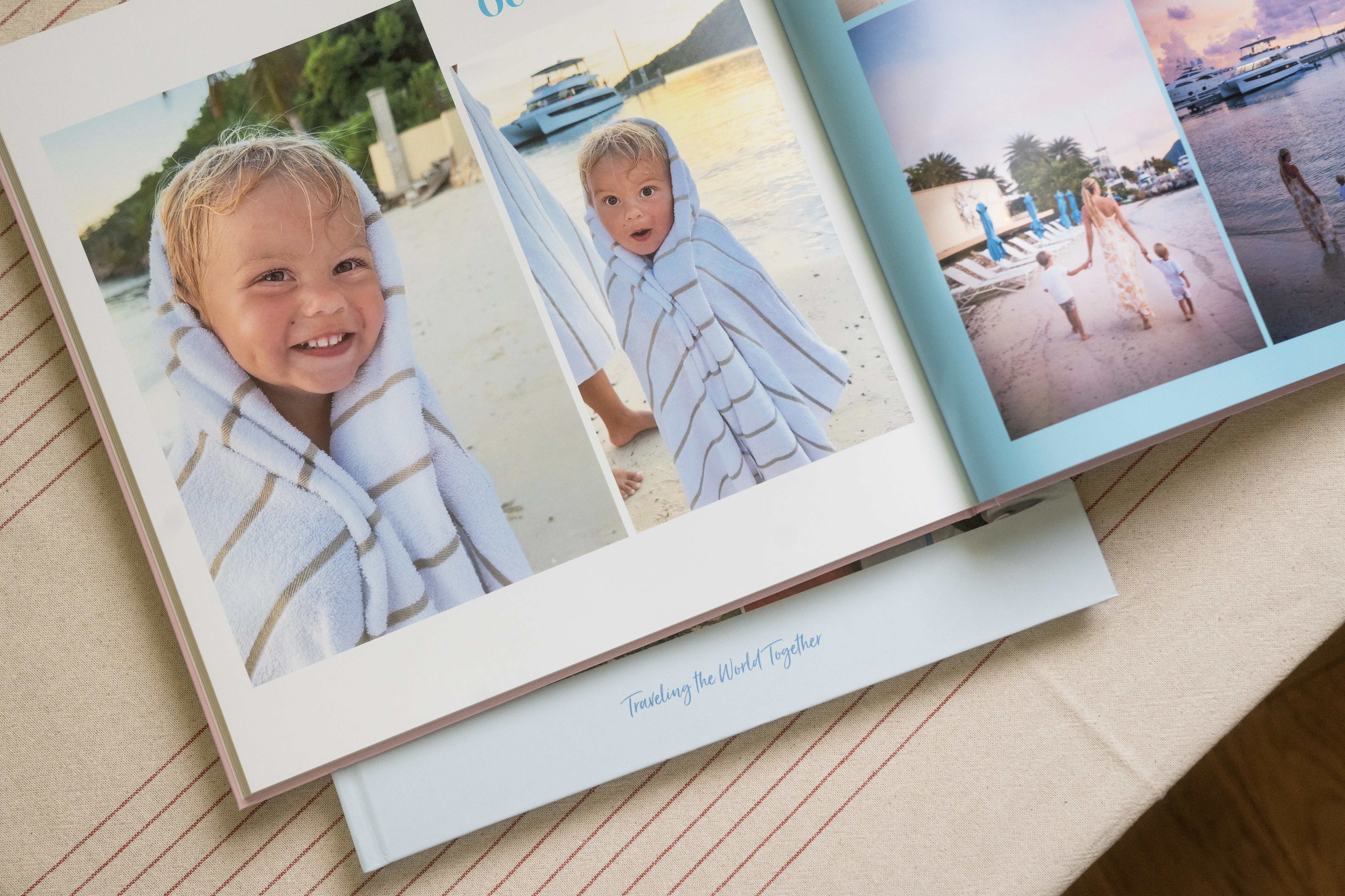 Open photo album on a table shows a child wrapped in a towel at the beach, with other beach and boat scenes in the background.