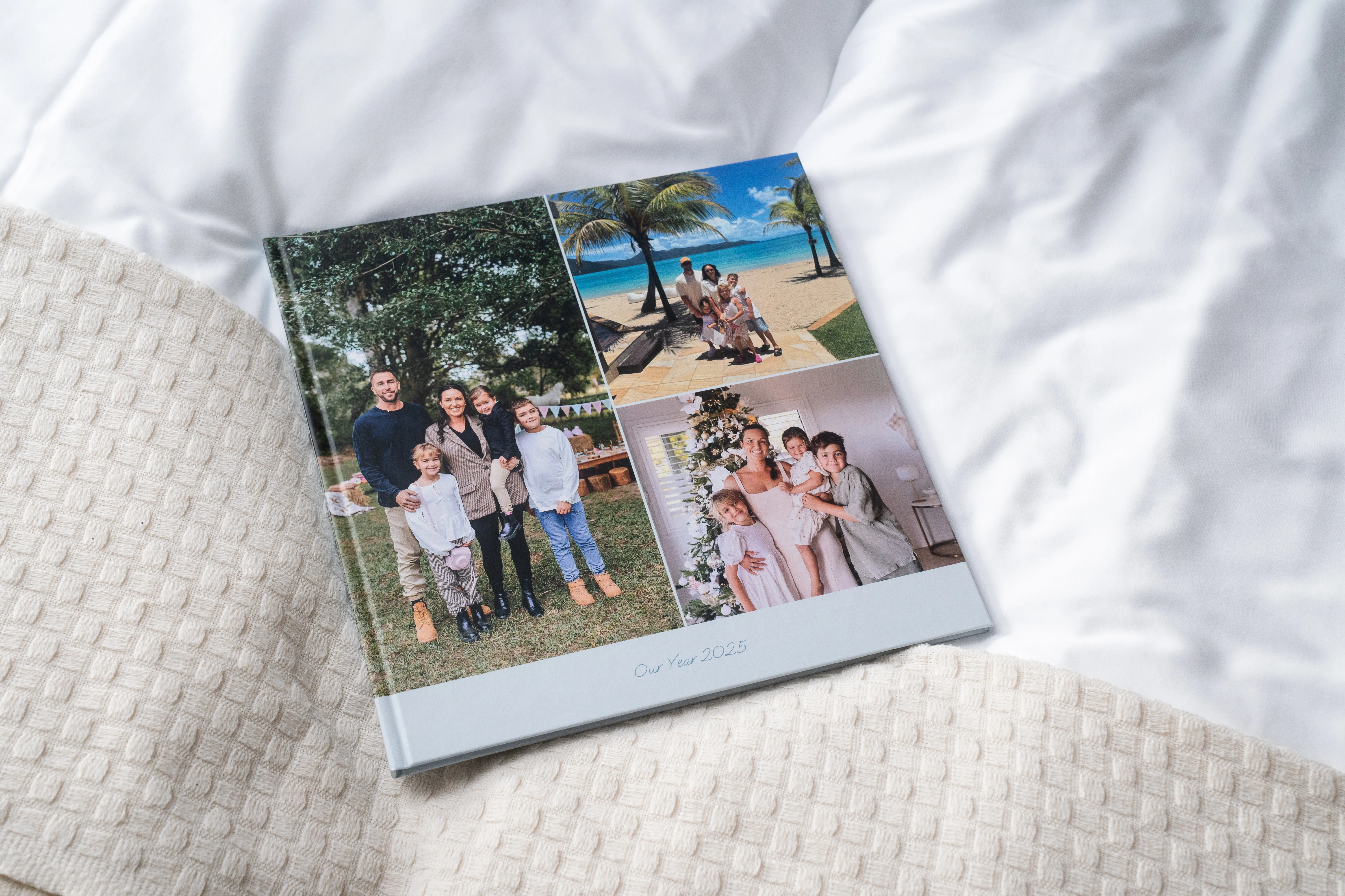 Hardcover Photo book on a textured blanket, featuring family pictures in various settings, titled "Our Year 2023."