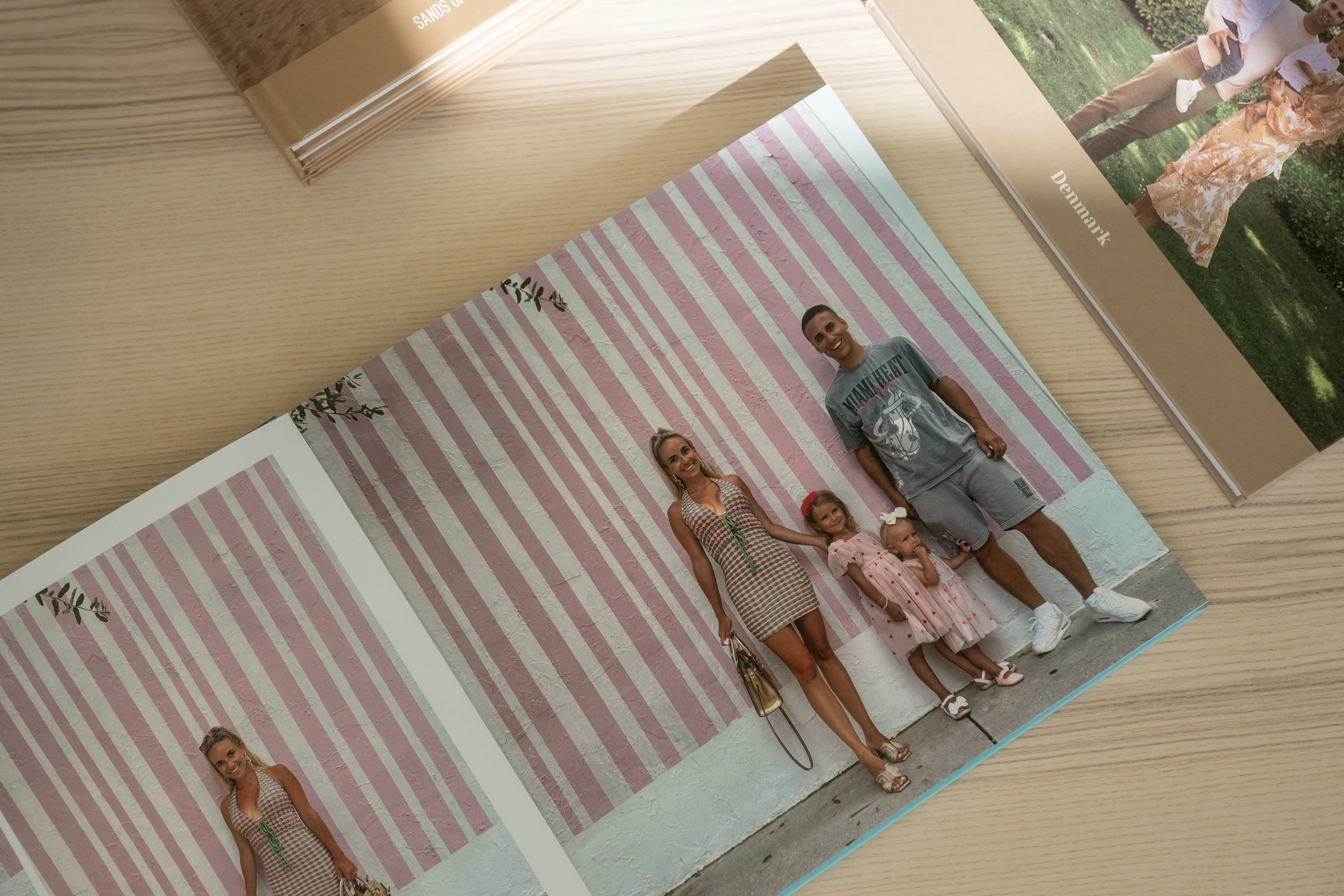 Open mother's day photo album on a wooden table, displaying a family posing against a pink-striped wall.