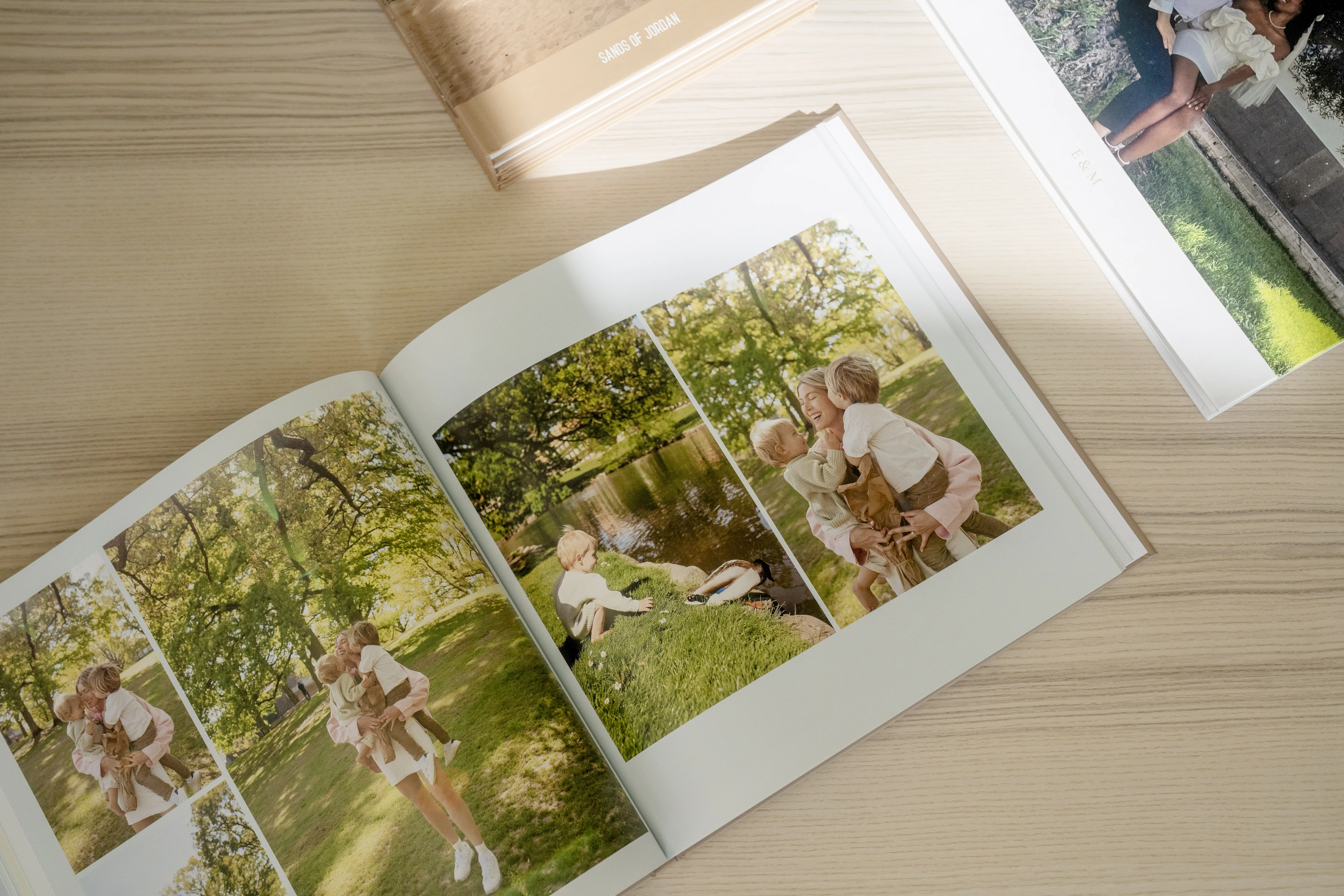 Offenes Fotoalbum auf einem Holztisch, das Familienfotos im Freien in einer Parklandschaft mit Bäumen und Gras zeigt. Ein weiteres Buch liegt daneben.