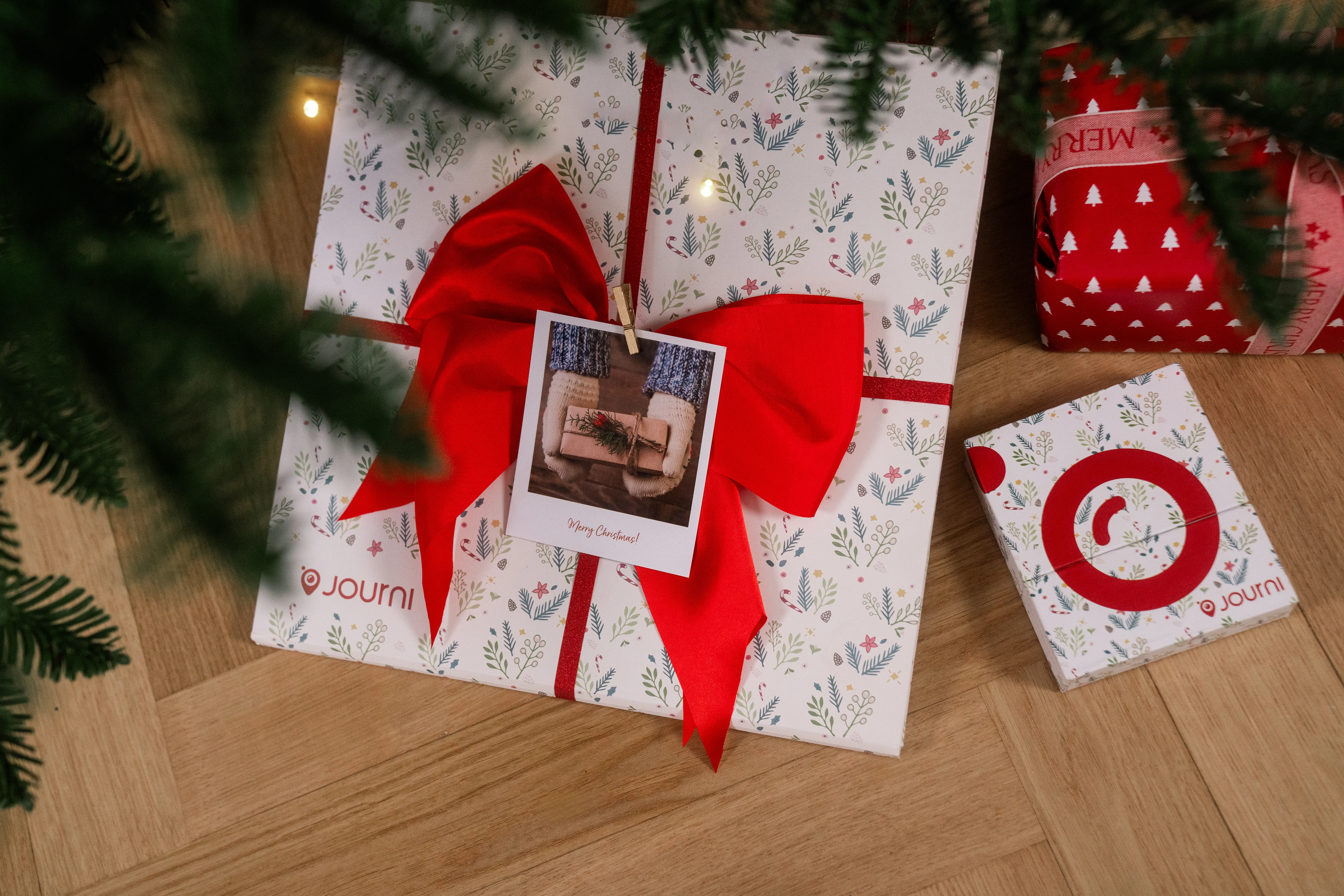 Ein Geschenk verpacktes Fotobuch unter einem Weihnachtsbaum, die Verpackung hat ein Muster aus Stechpalmen und Weihnachtsternen.