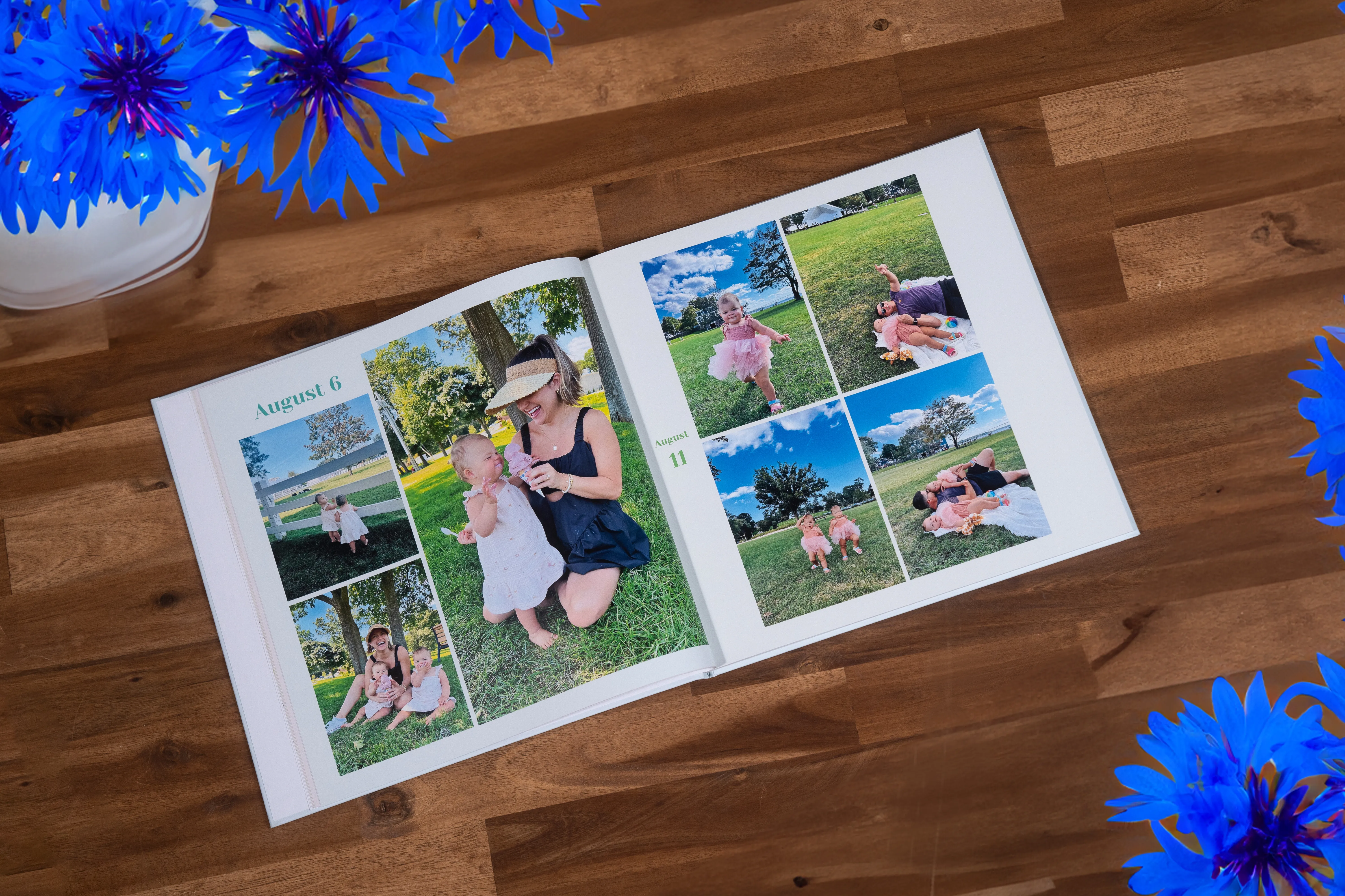 Open photo album on a wooden table, displaying outdoor family photos. Blue flowers decorate the corners.