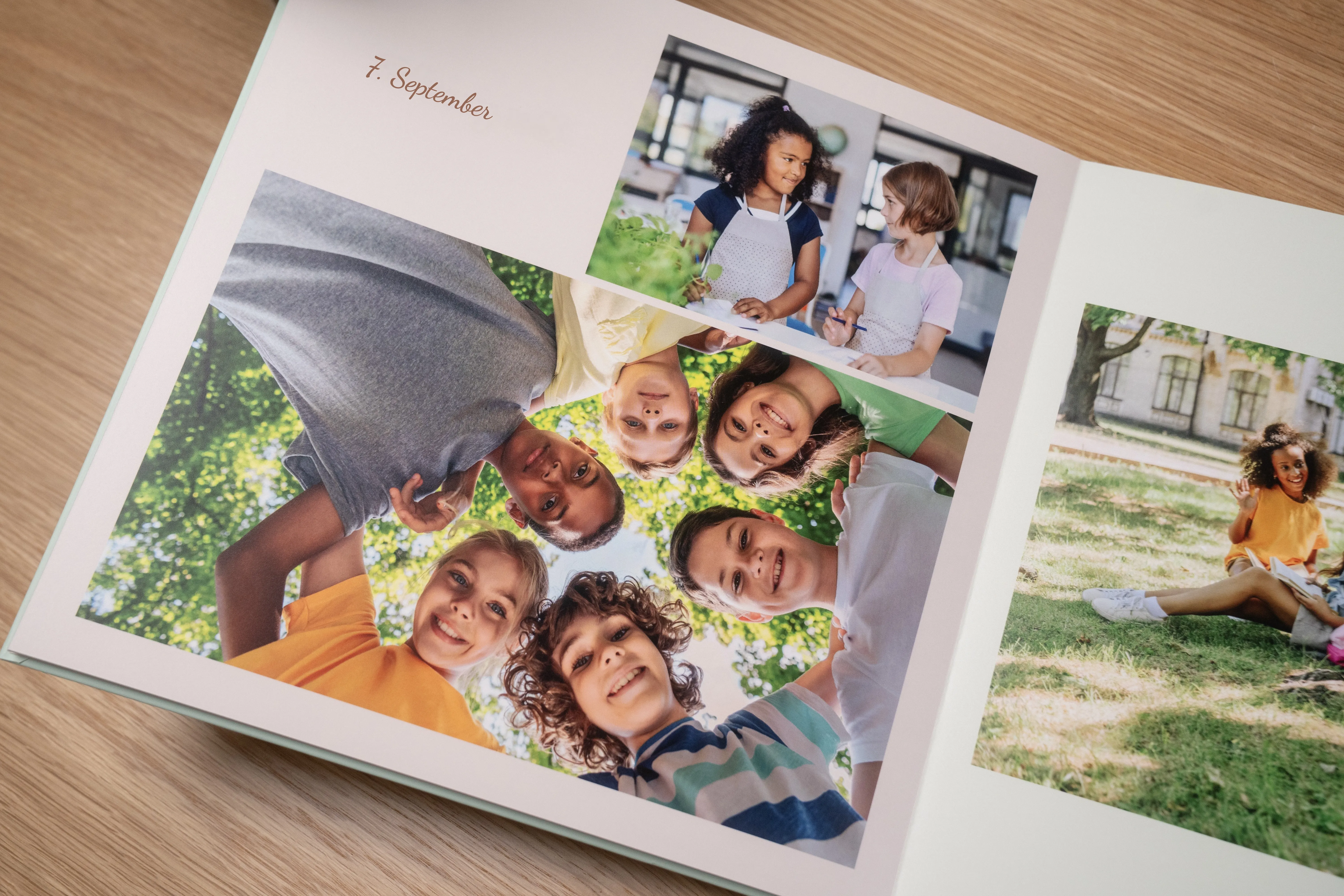 Offenes Fotobuch mit Kindern, die im Freien im Kreis lächeln, und zwei Kindern, die im Gras sitzen, datiert auf den 7. September.