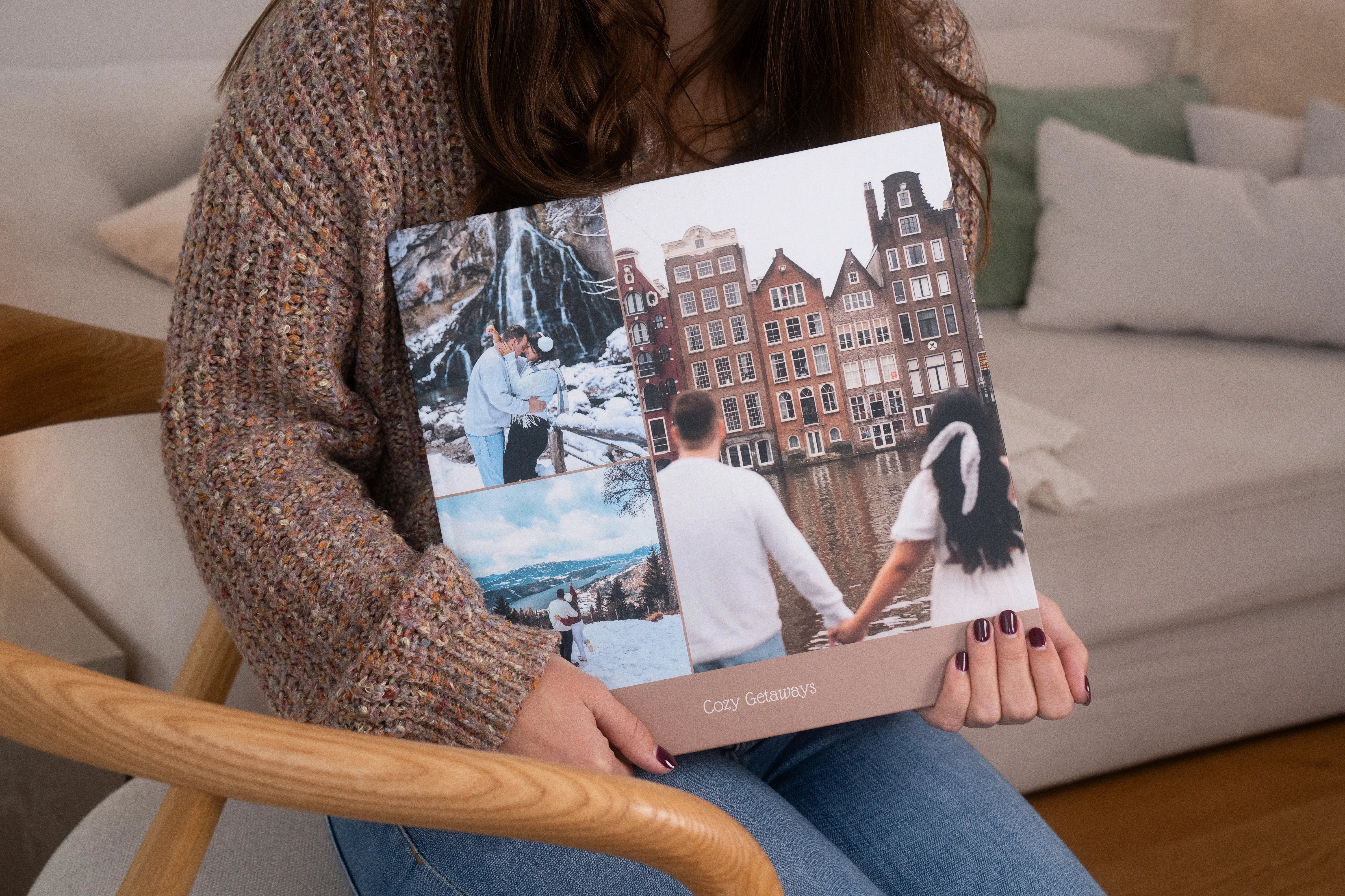 A person sitting on a chair holds a photo book featuring travel images, including a couple holding hands and scenic views of buildings and landscapes.