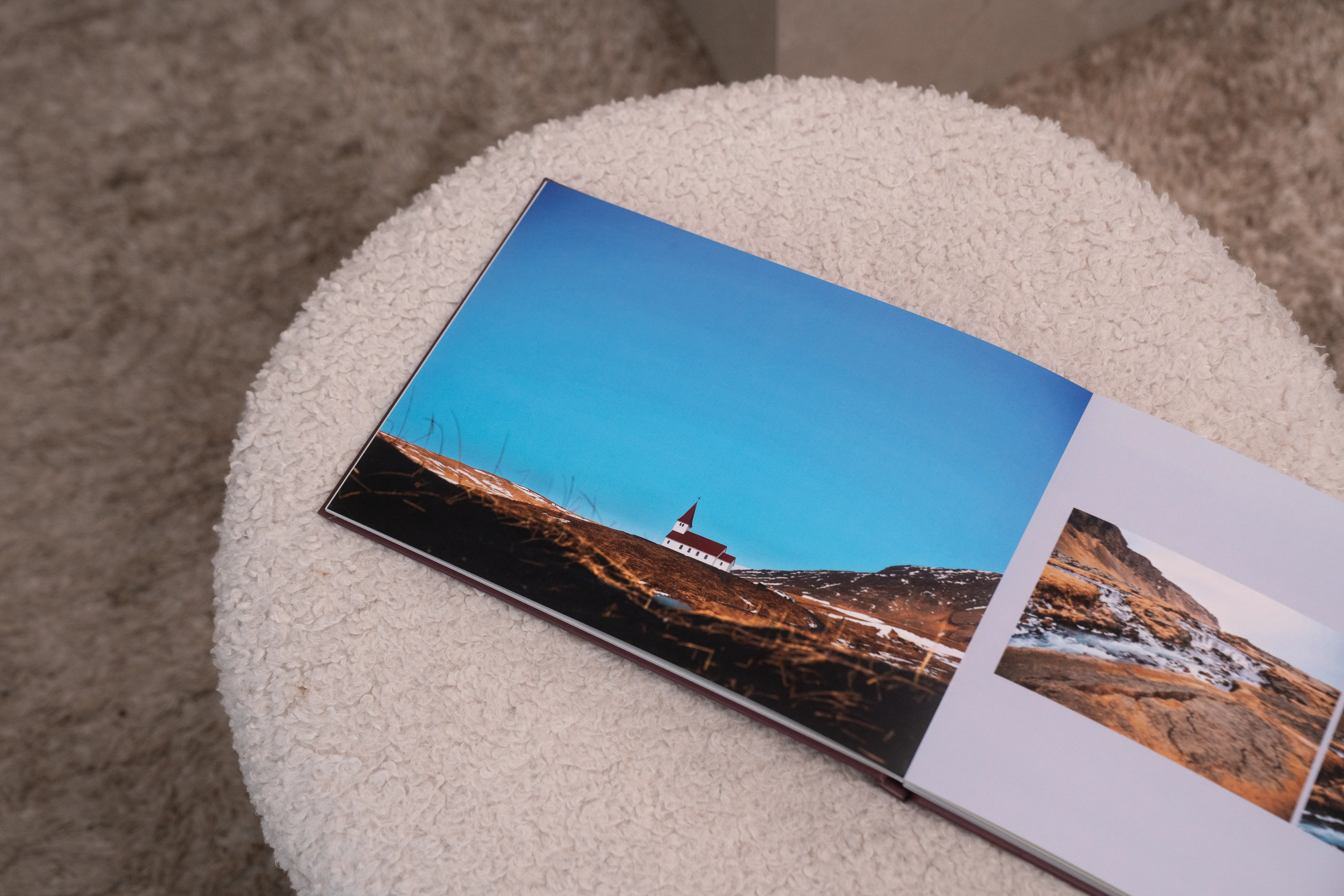 Offenes Layflat-Fotobuch auf einem weißen Hocker mit einem ganzseitigen Foto einer Winterlandschaft.
