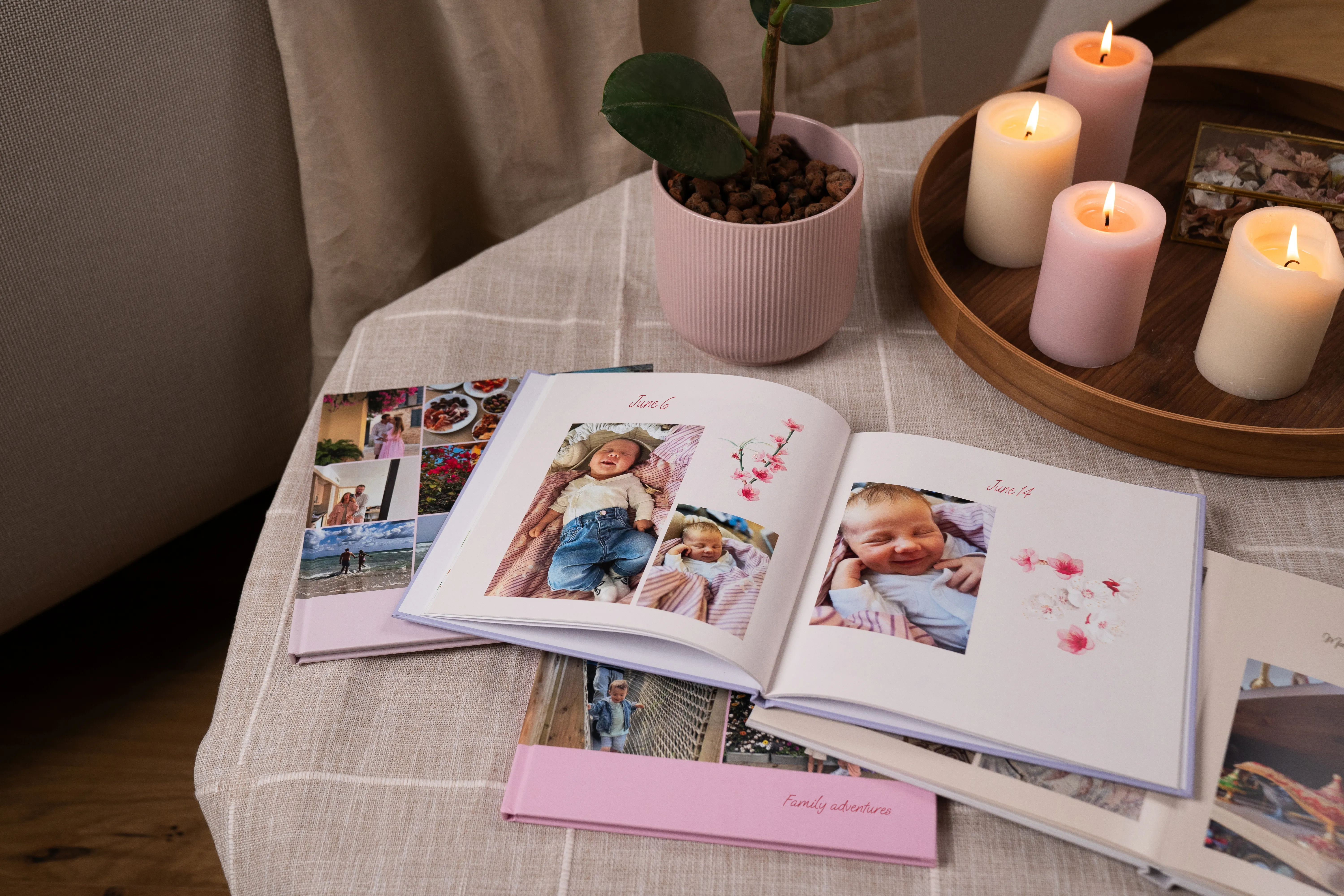 Geöffnete Fotoalben auf einem Tisch mit brennenden Kerzen und einer Topfpflanze, die Familienfotos und florale Motive zeigen.