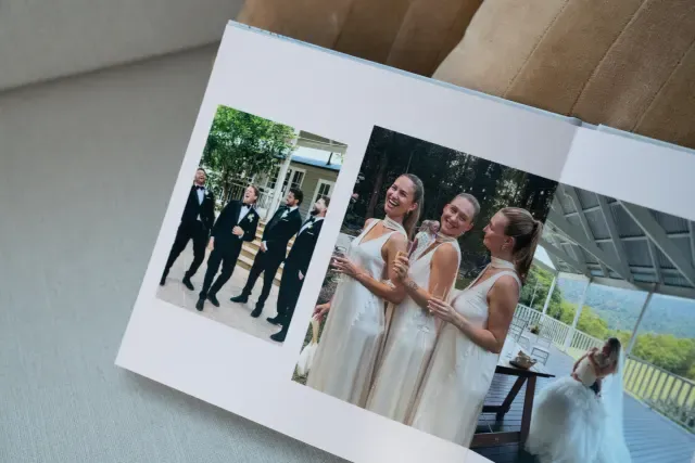 Open layflat photo album showing two images: one of four groomsmen in suits, and another of three bridesmaids in gowns, with a bride in the distance.