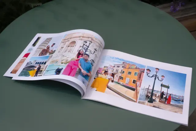Open softcvoer photo book on a green table, showing colorful travel images of landmarks and people in various settings.