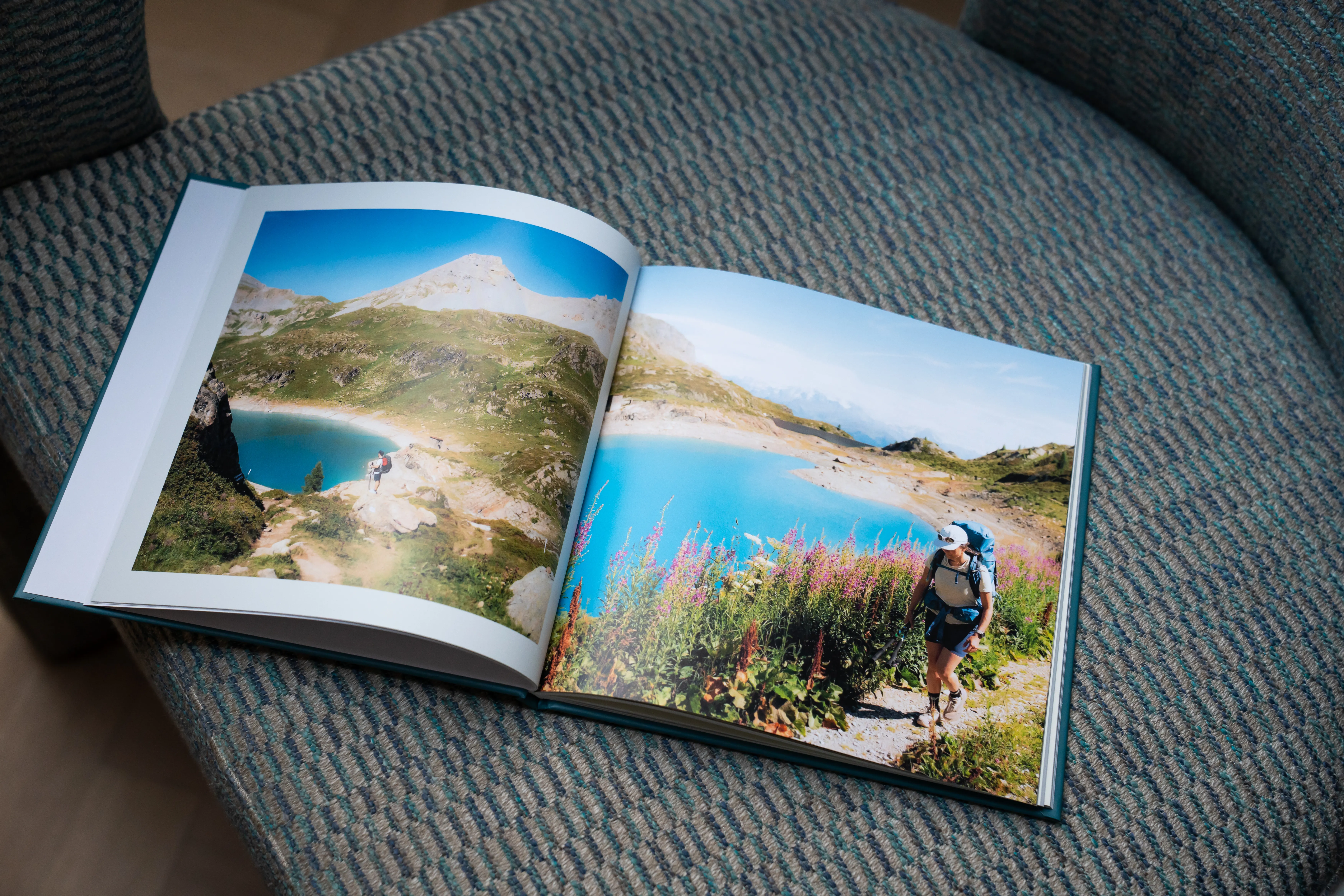 Ein auf einem Stuhl aufgeschlagenes Fotobuch, das lebendige Bilder einer Wandererin an einem türkisfarbenen Bergsee und inmitten üppiger Vegetation zeigt.
