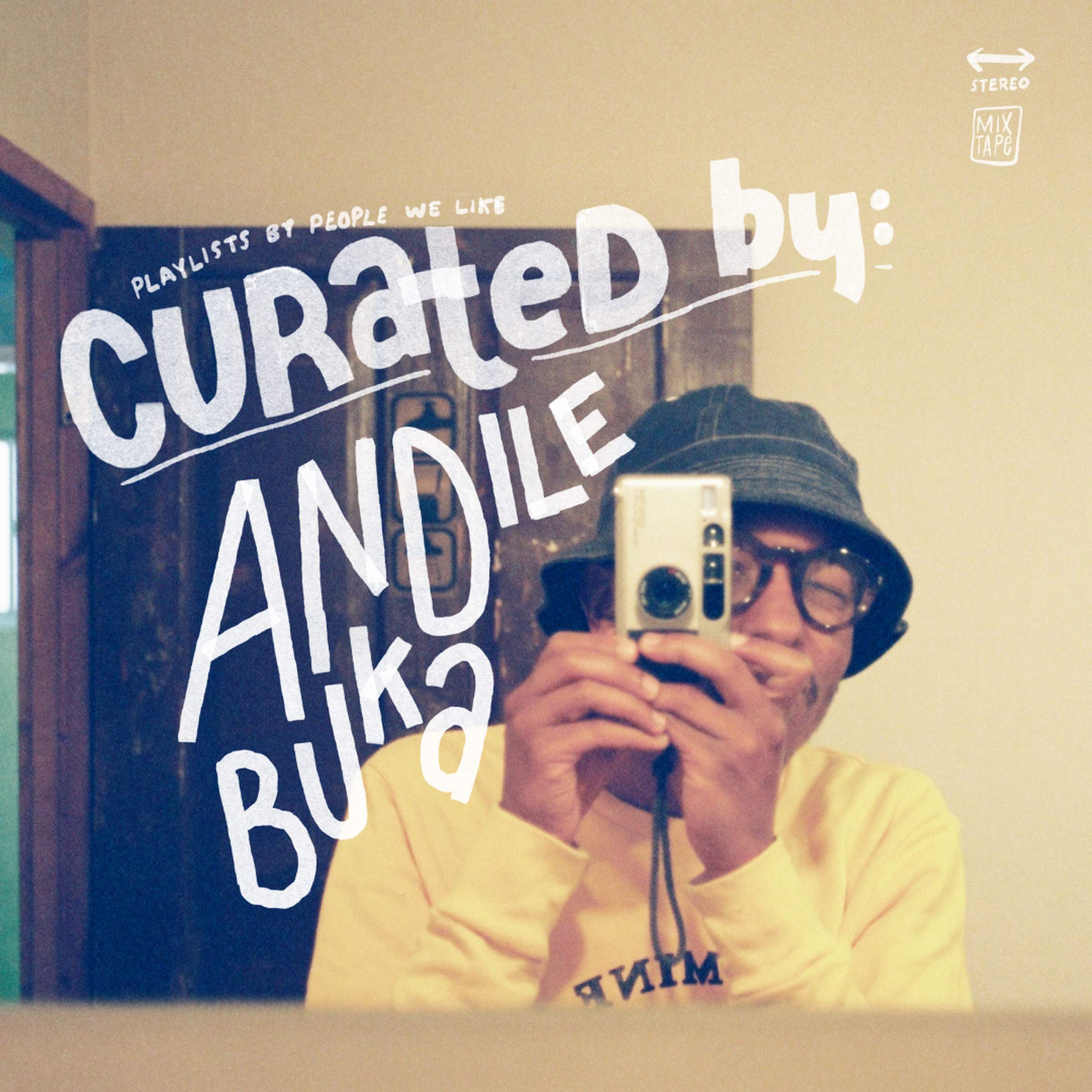 Person in a yellow sweater and bucket hat takes a mirror selfie with a camera. Text reads "Curated by: Andile Buka."