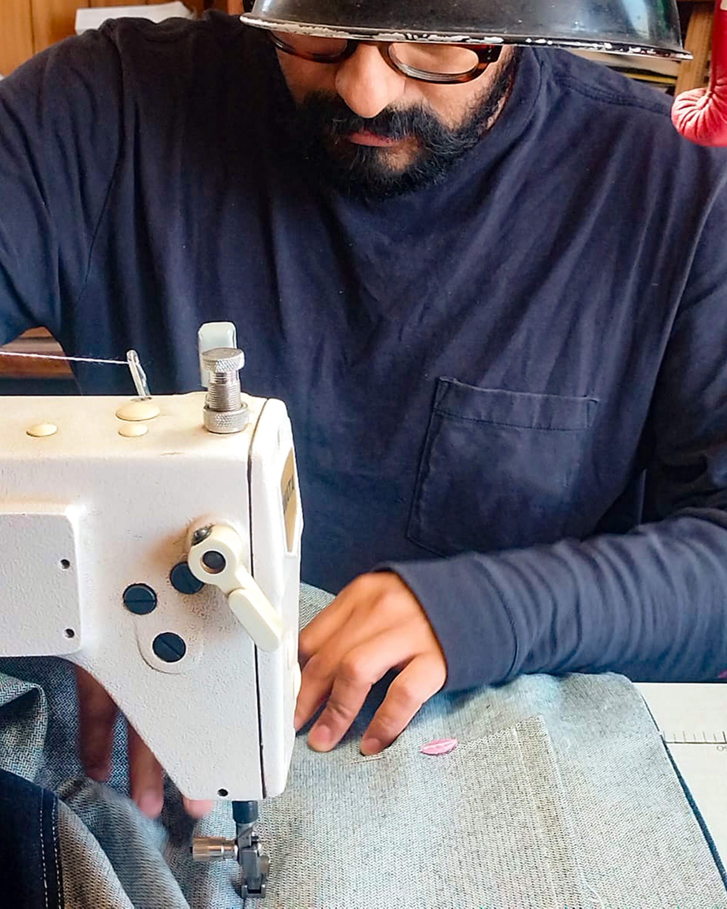 Person sewing fabric with a sewing machine, wearing glasses and a dark long-sleeve shirt, focused on their work.