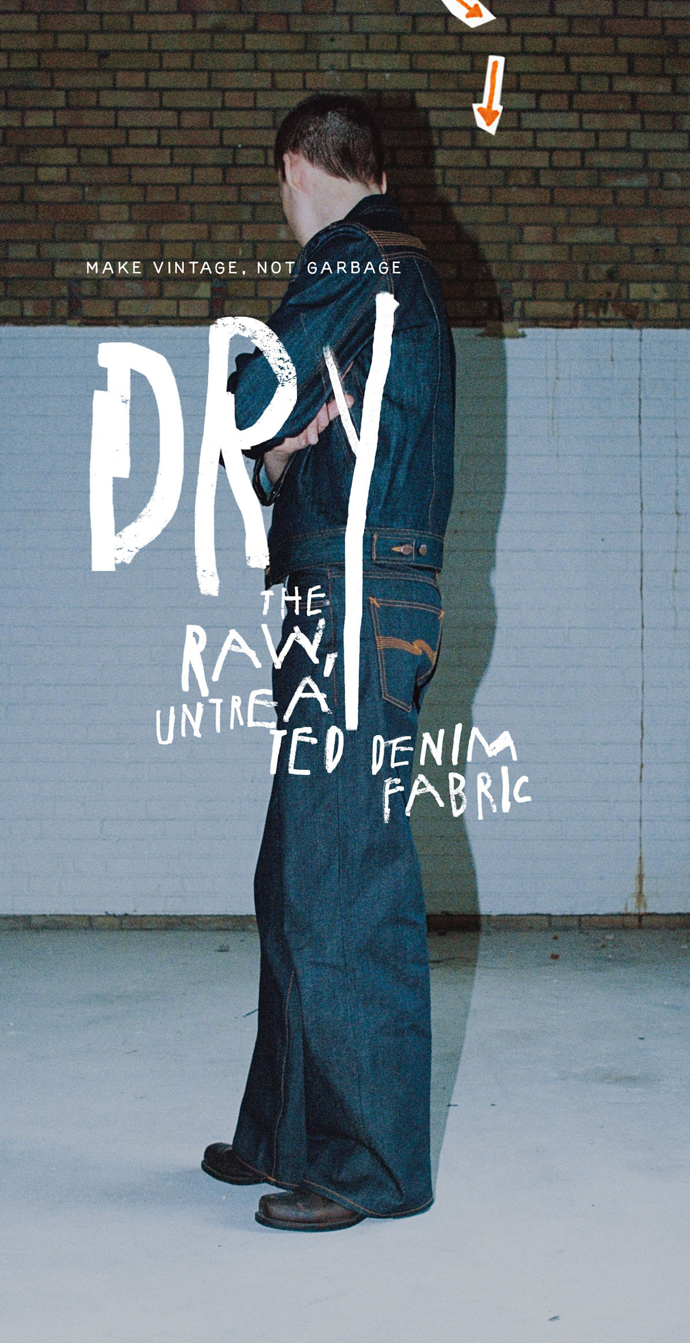 Person in dark denim outfit stands against a brick and white wall. Text reads: "DRY: The Raw, Untreated Denim Fabric."