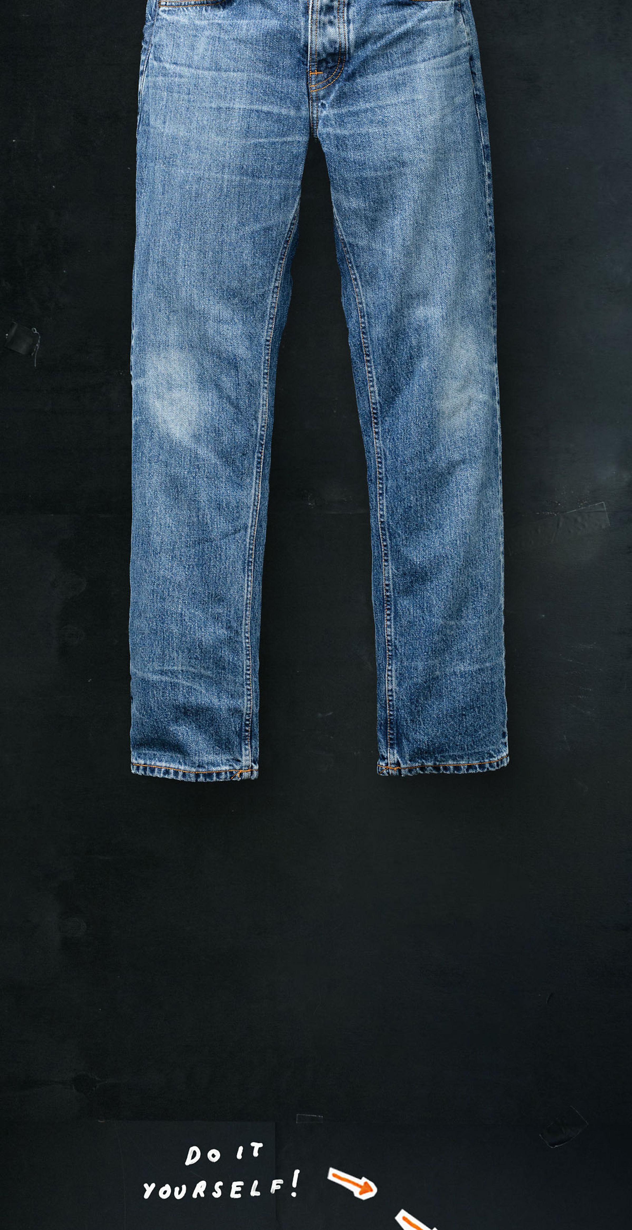 Blue jeans hanging against a dark background with "Do It Yourself!" written below in white text and arrows pointing upwards.