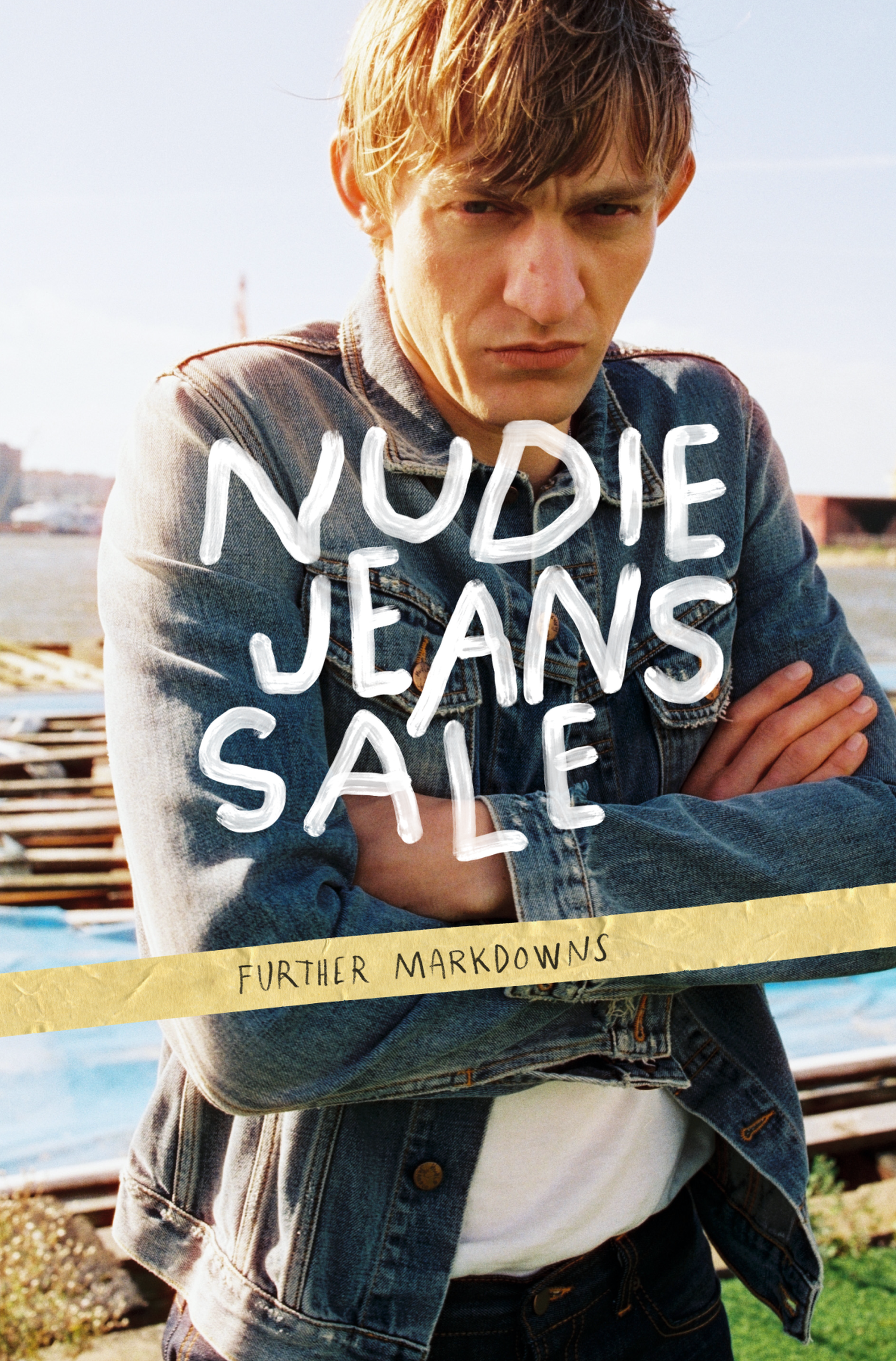 Person in a denim jacket standing by water, arms crossed, with text reading "Nudie Jeans Sale" and "Further Markdowns."