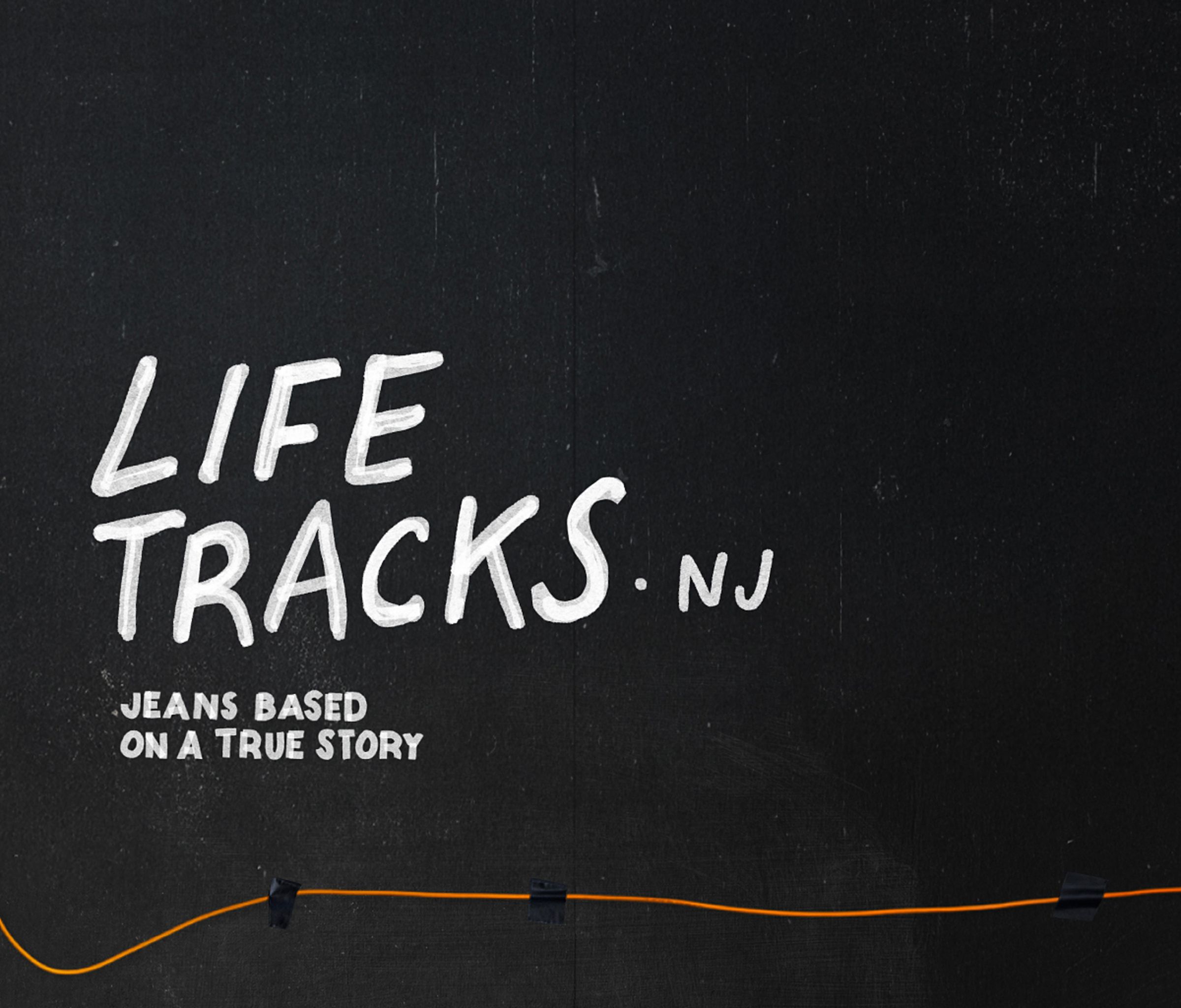 Blackboard with white text reading "Life Tracks NJ" and "Jeans Based on a True Story," with an orange wire at the bottom.