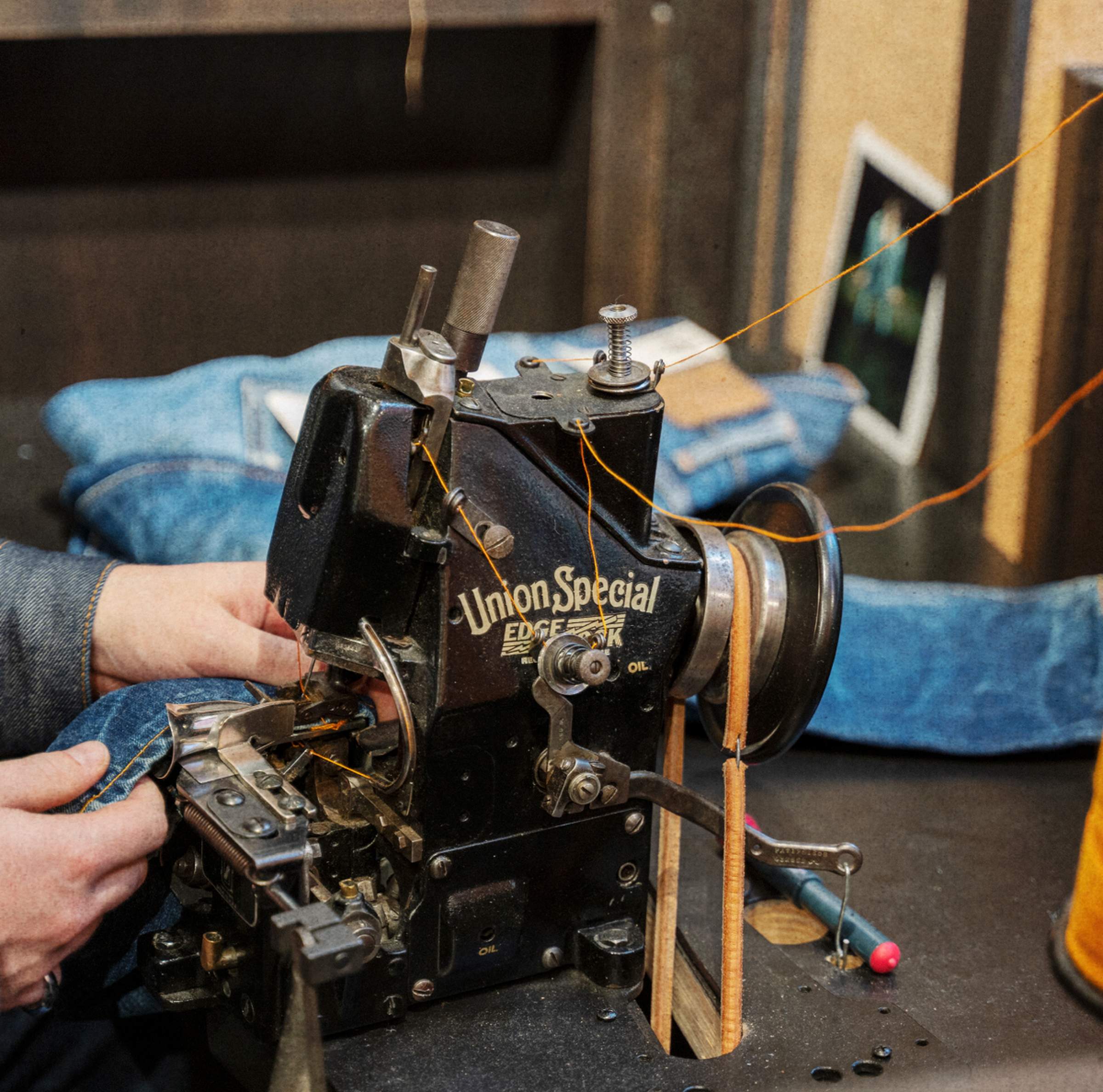 Person using a vintage Union Special sewing machine to stitch denim fabric, with threads visible and jeans partially in view.
