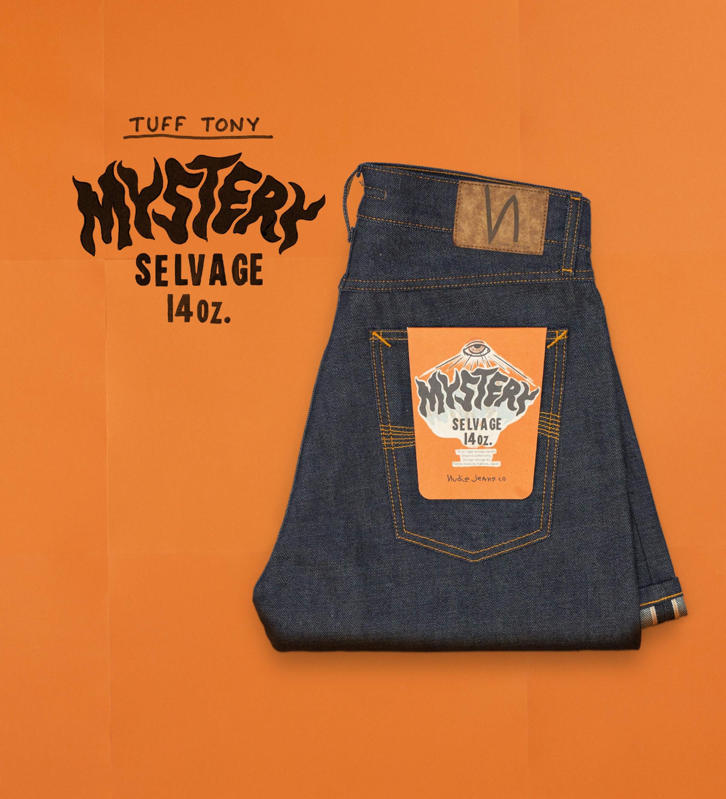 Folded pair of dark blue jeans with a colorful label on the back pocket, placed on an orange background. Mystery Selvage. Nudie Jeans