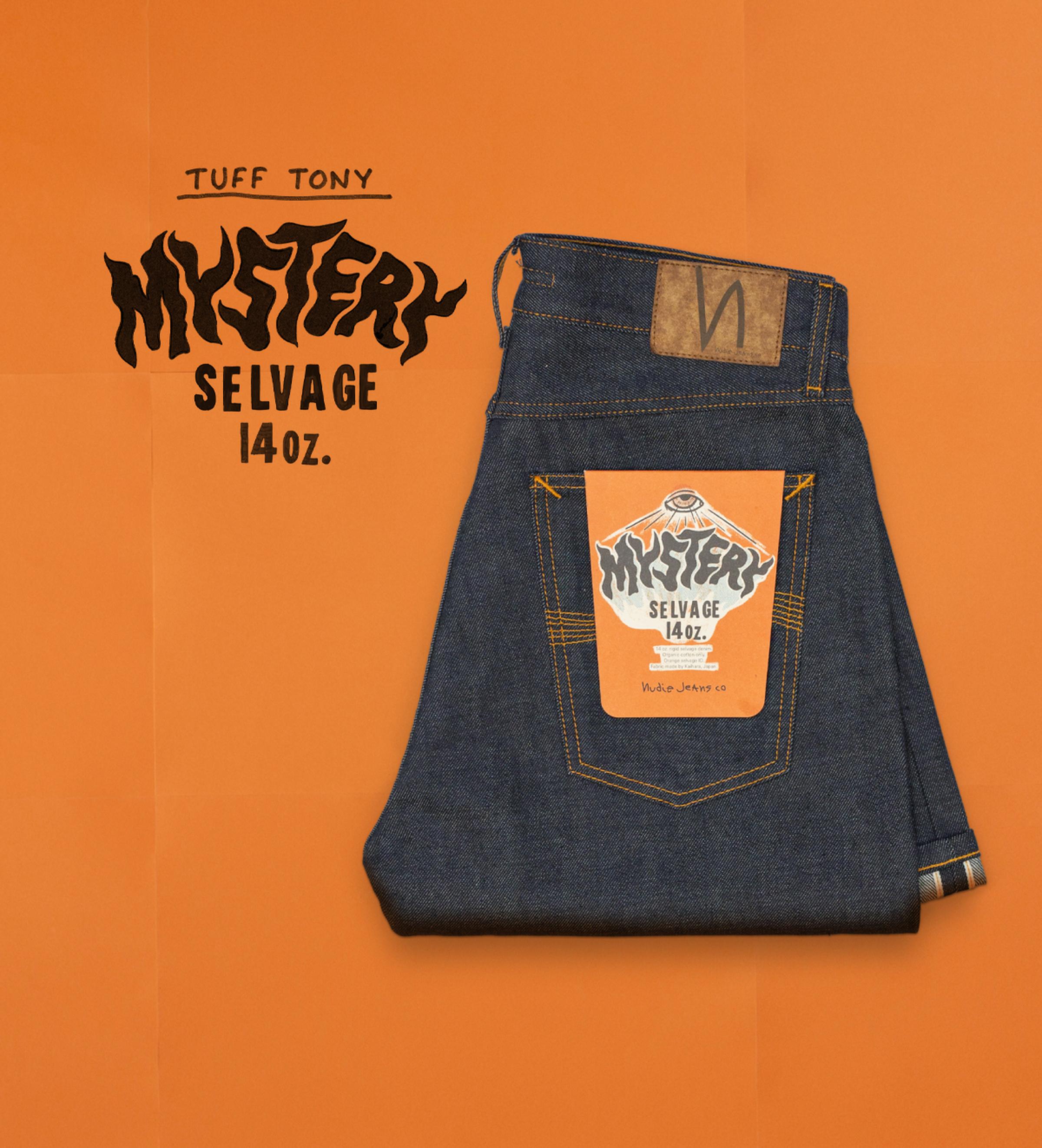 Folded pair of dark blue jeans with a colorful label on the back pocket, placed on an orange background. Mystery Selvage. Nudie Jeans