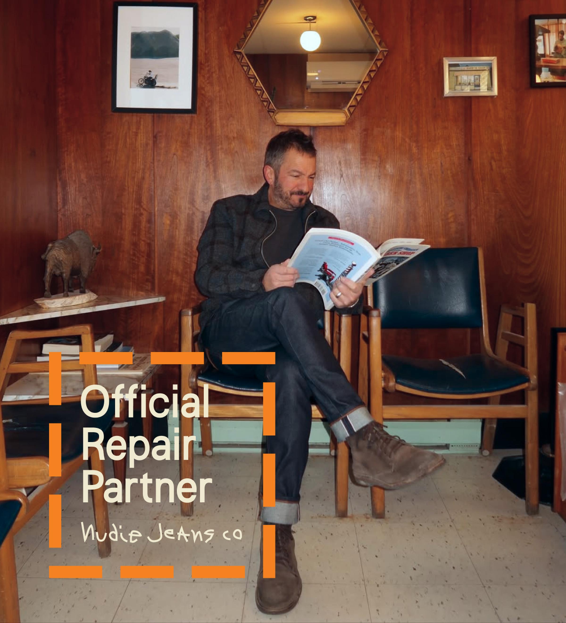 Man in a cozy room, seated and reading a magazine. Text overlay: "Official Repair Partner Nudie Jeans Co."