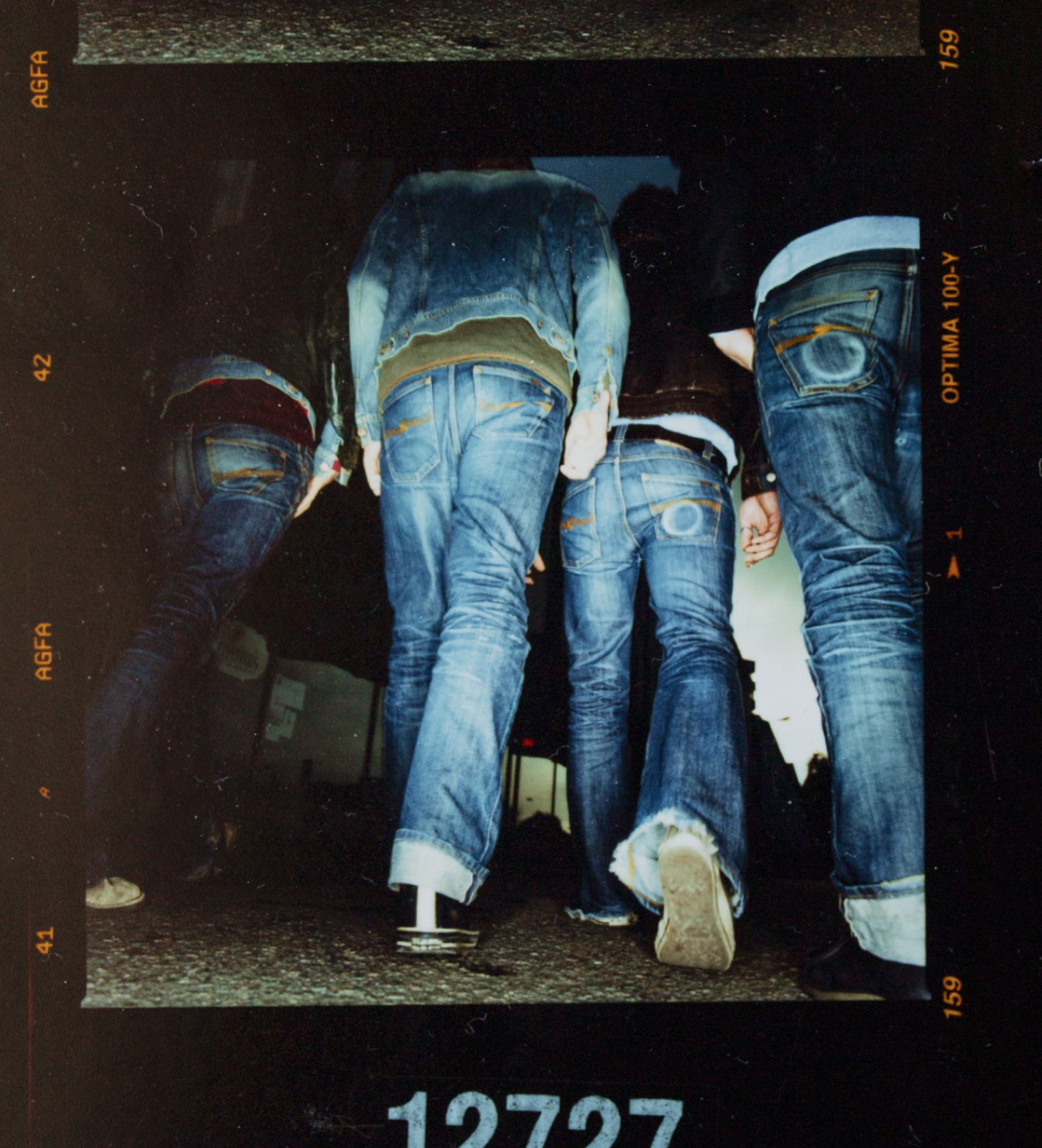 Four people wearing nudie jeans and jackets walking on a dark street, photographed from a low angle.
