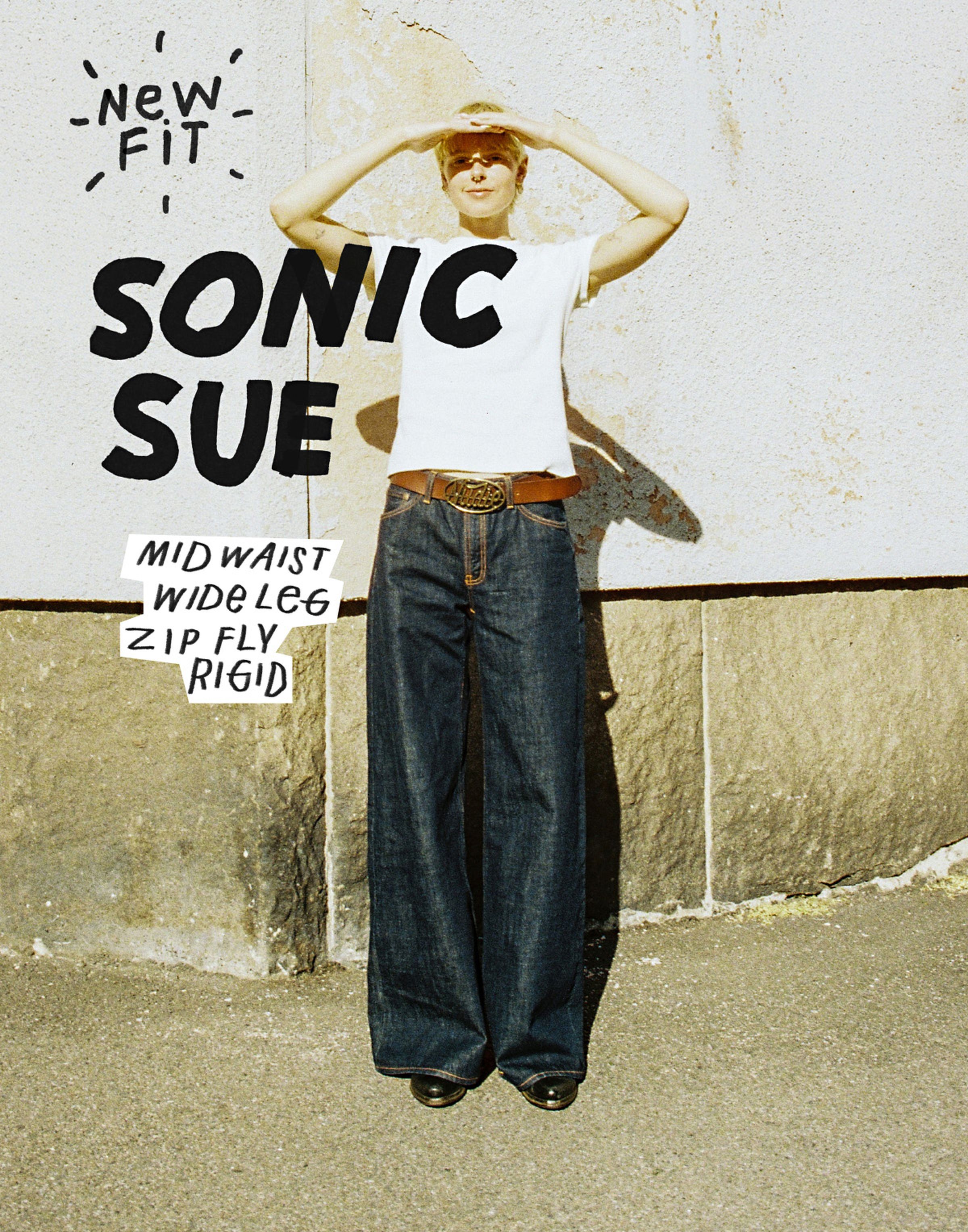 Person in wide-leg jeans and white shirt shields eyes from sunlight, stands against a textured wall. Text reads "Sonic Sue" and details about jeans.