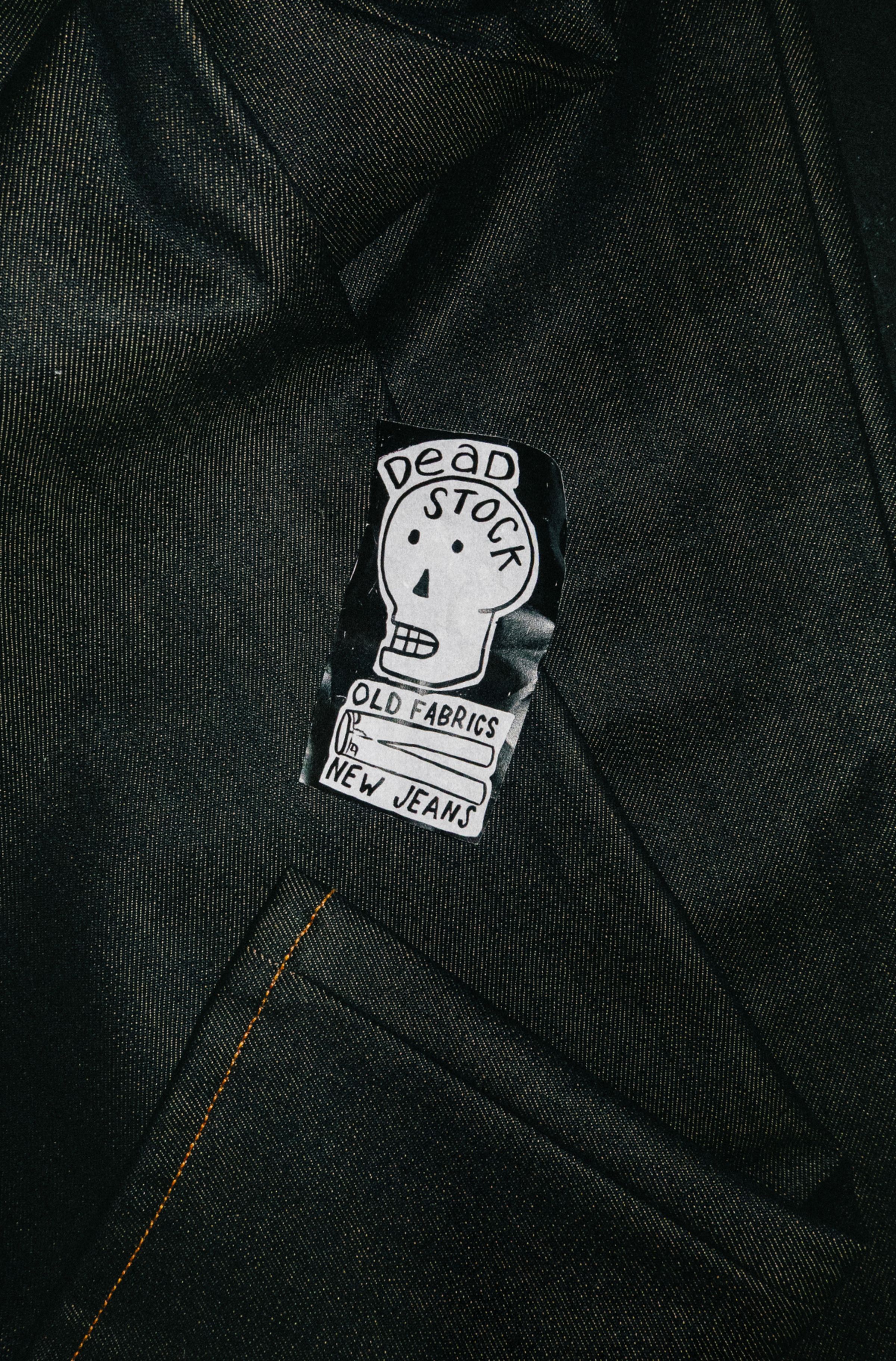 A black fabric patch with a white skull illustration and the text "Dead Stock, Old Fabrics, New Jeans" sewn onto dark denim.
