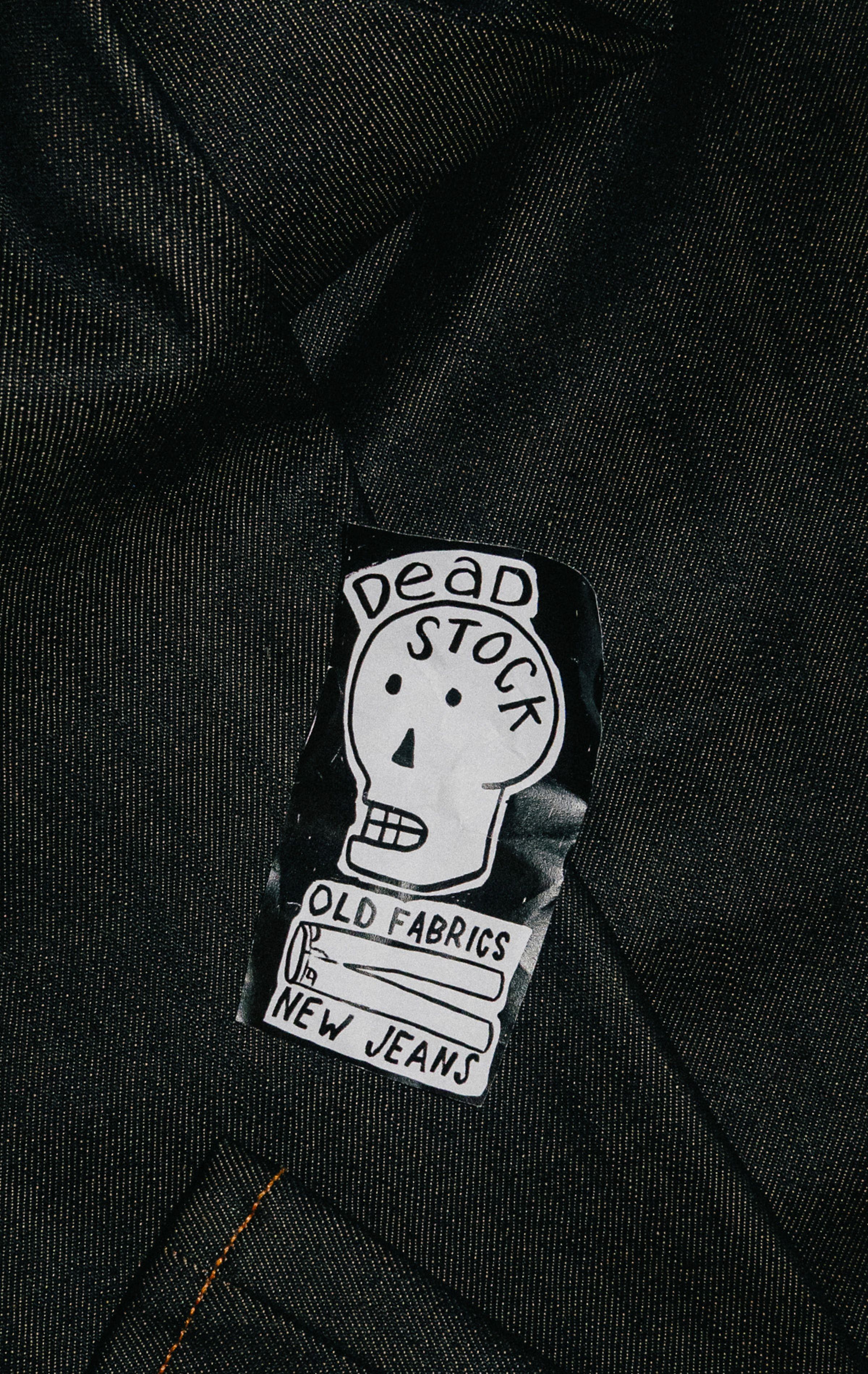 Sticker on denim with a skull drawing labeled "Dead Stock," and text "Old Fabrics, New Jeans."