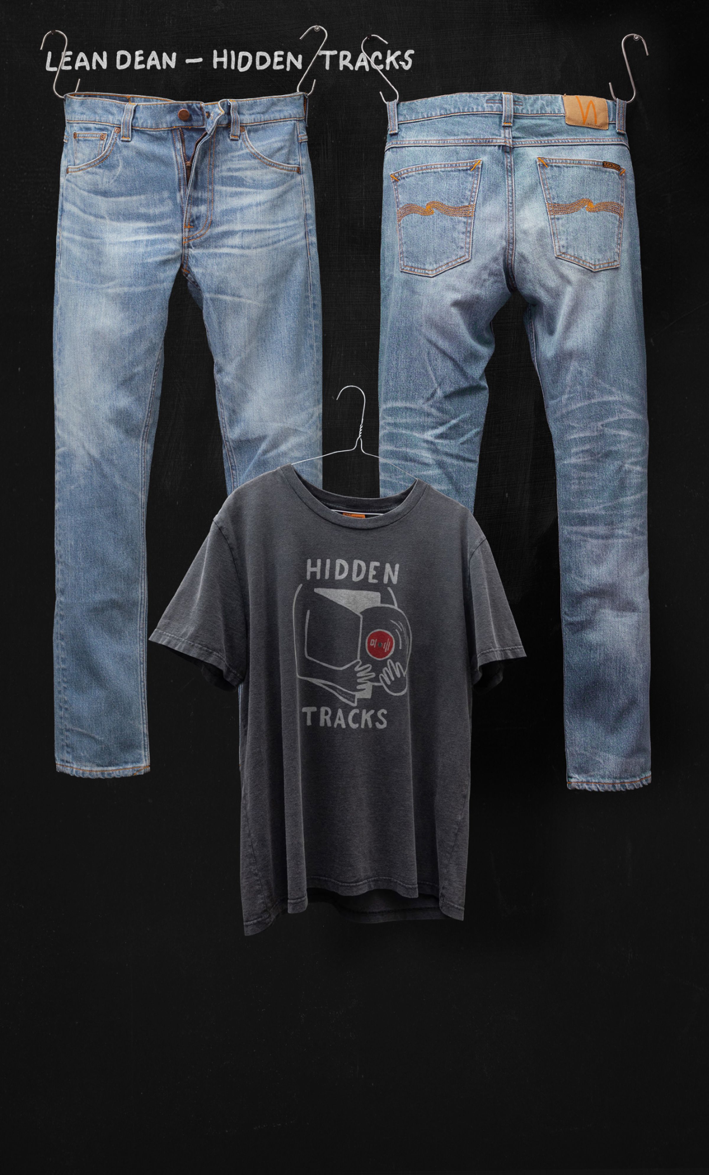 Two pairs of blue jeans and a black T-shirt with "Hidden Tracks" text and graphic, hanging on a black background.
