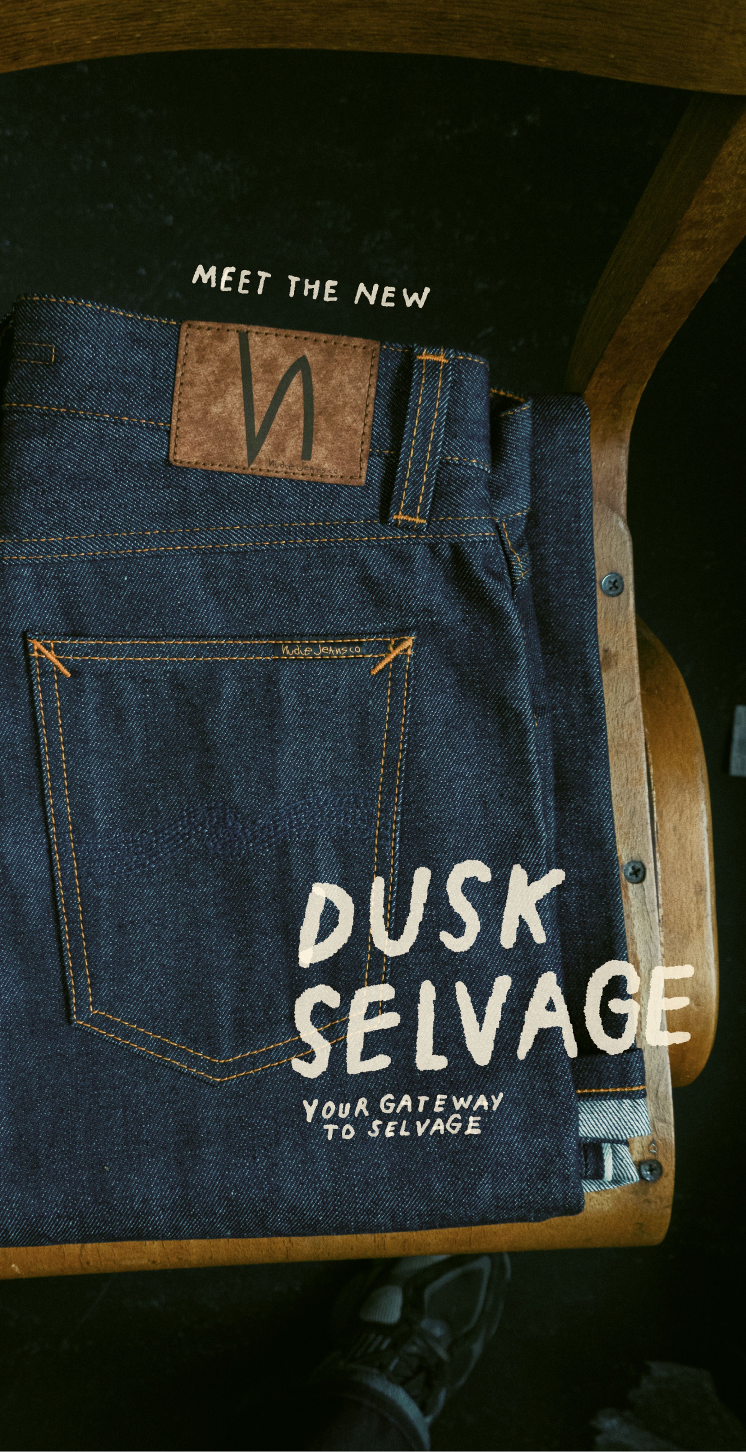RAW selvage denim jeans with brown leather patch on a wooden chair. Text reads, "Meet the New Dusk Selvage: Your Gateway to Selvage."
