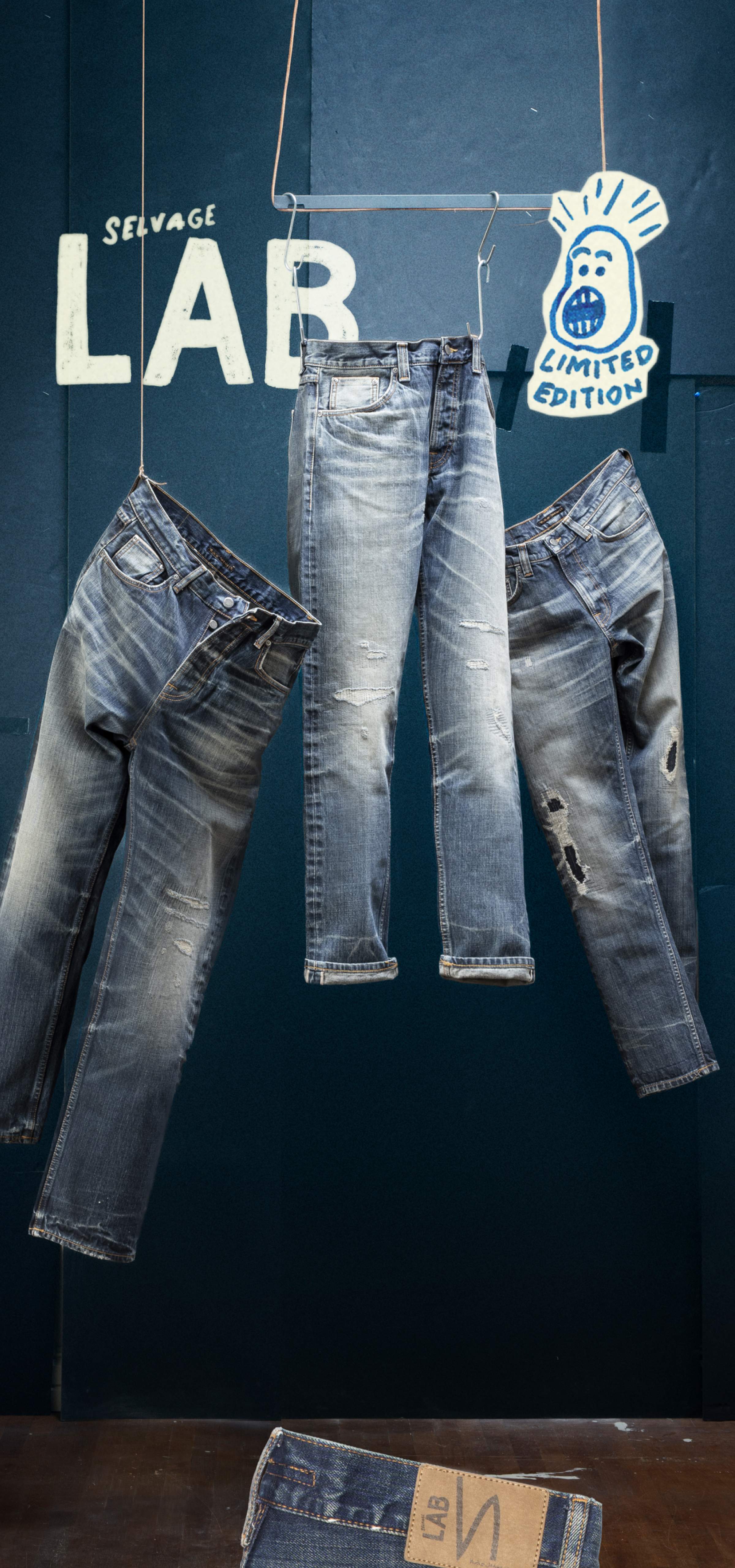 Three pairs of distressed jeans hang against a dark backdrop with "Selvage LAB" text and illustrated graphics saying Limited Edition