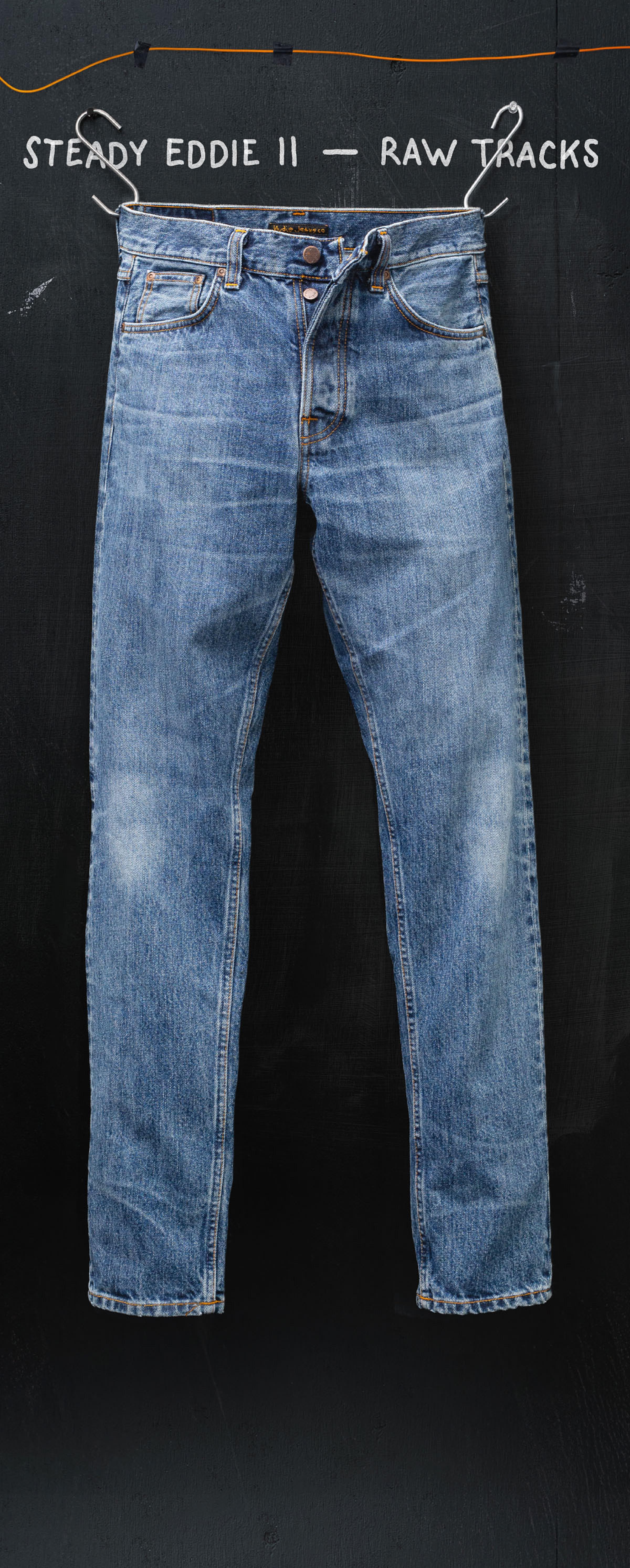 A pair of blue jeans with a belt, labeled "Steady Eddie II - Raw Tracks," hangs against a dark background.