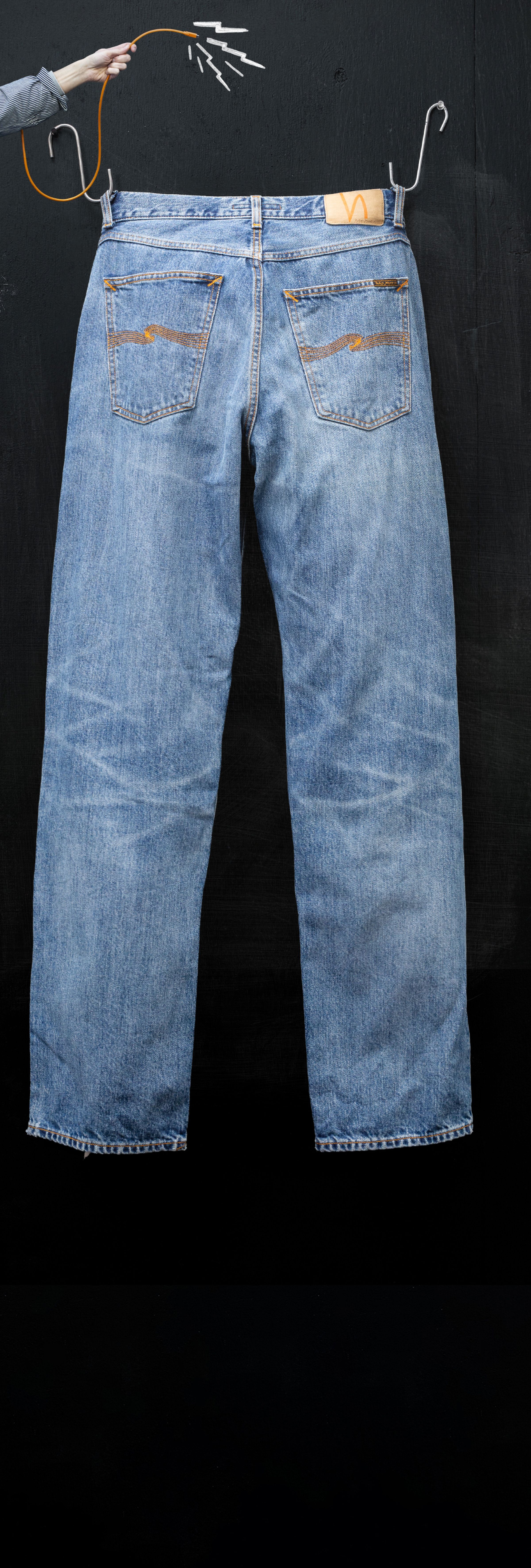 Blue jeans hanging on a wire hanger against a dark background, with a hand holding the hanger.