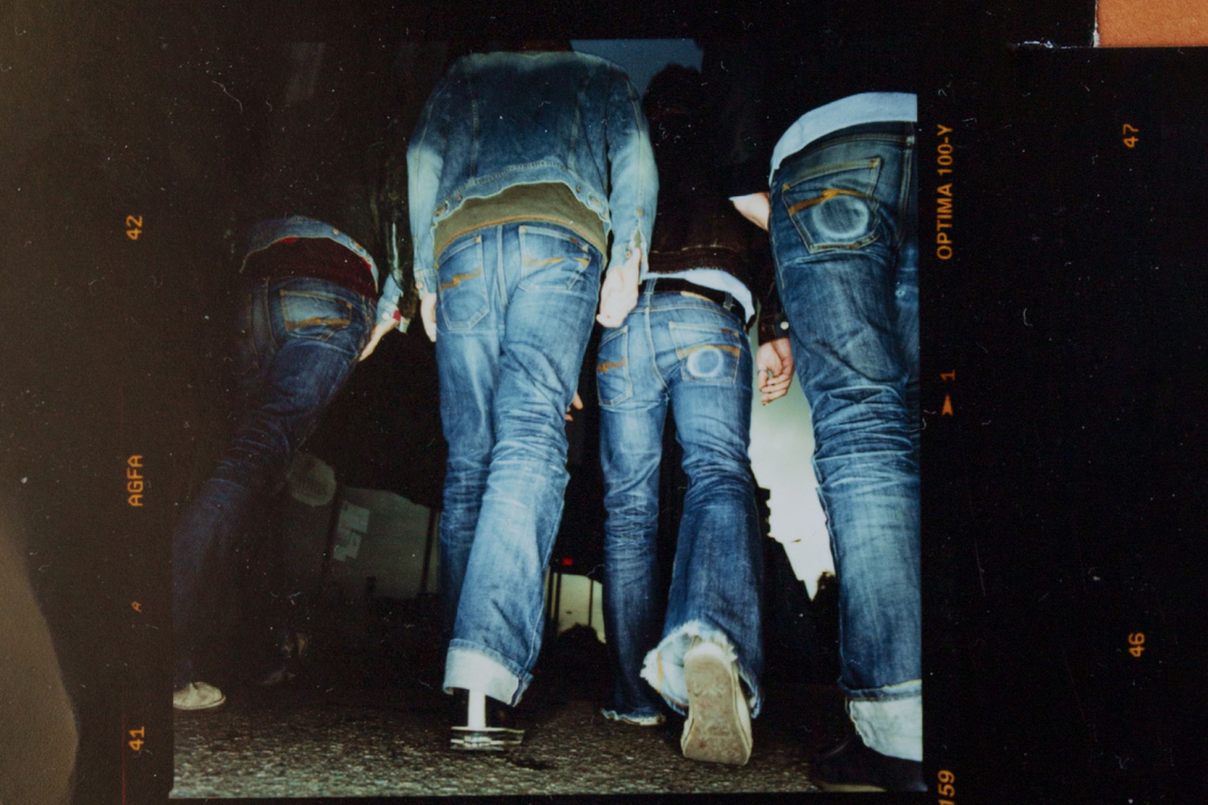Four people wearing nudie jeans and jackets walking on a dark street, photographed from a low angle.