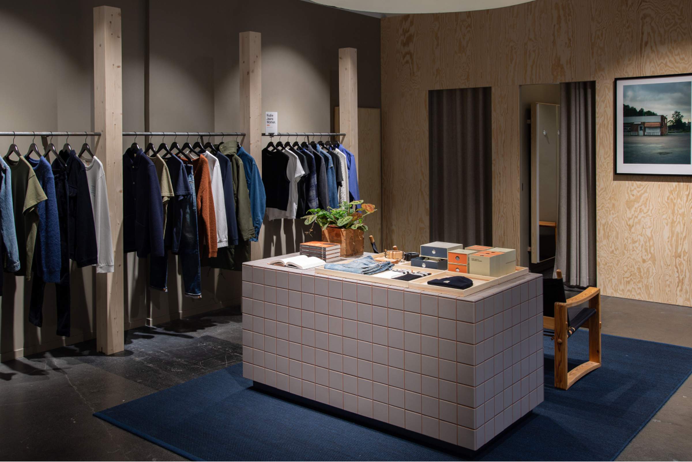 Interior of the refurbished Nudie Jeans Skånegatan Repair Shop with clothing racks, tiled display counter, and fitting area