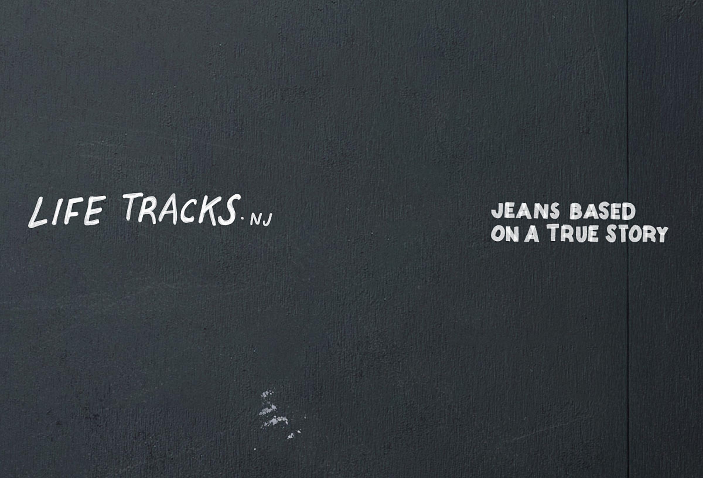 Dark wall with white text: "LIFE TRACKS. NJ" on the left and "JEANS BASED ON A TRUE STORY" on the right.