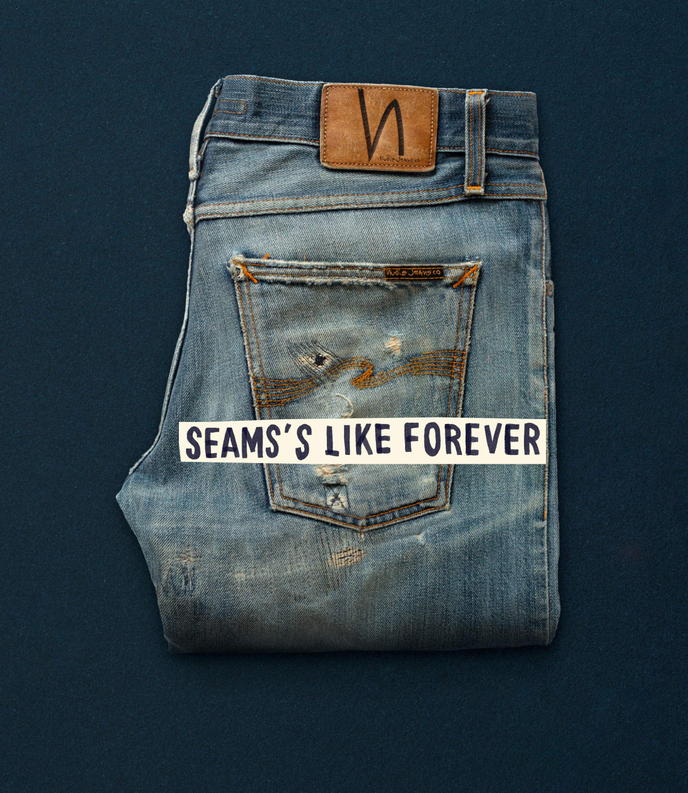 Folded distressed jeans with visible wear and a leather patch, placed on a dark surface. Text overlay reads, "SEAMS'S LIKE FOREVER."