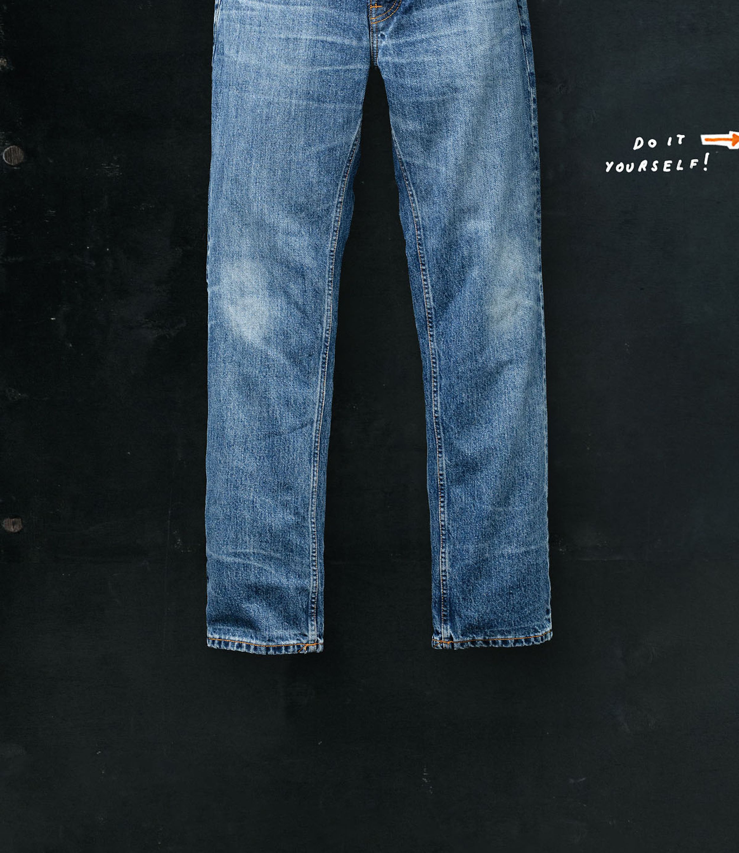 Faded blue jeans hanging against a dark wall with the text "Do It Yourself!" written in white and orange in the top right corner.