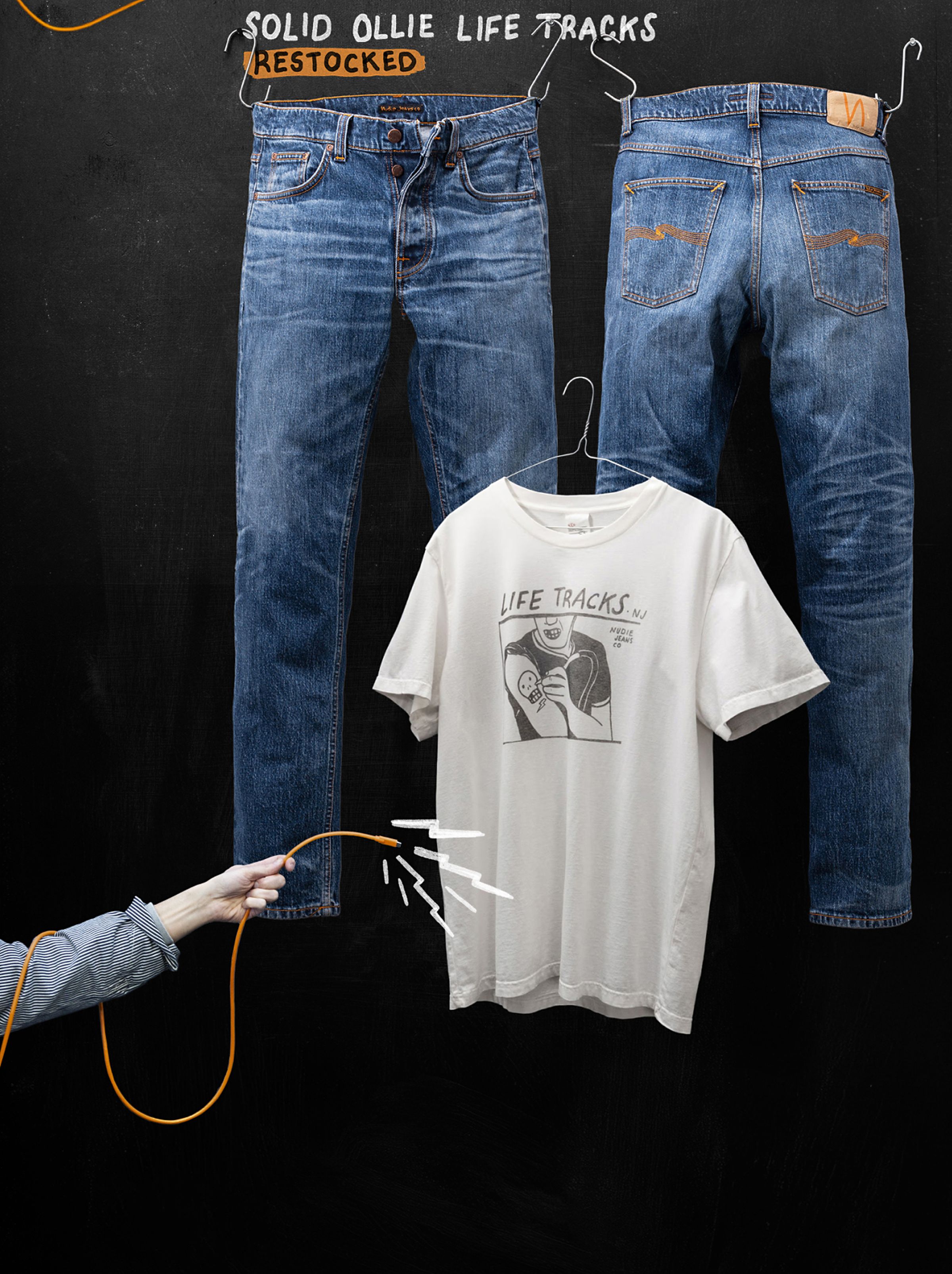 Jeans and a graphic T-shirt hanging against a black background. A hand holds an orange cord, with text above: "Solid Ollie Life Tracks Restocked."
