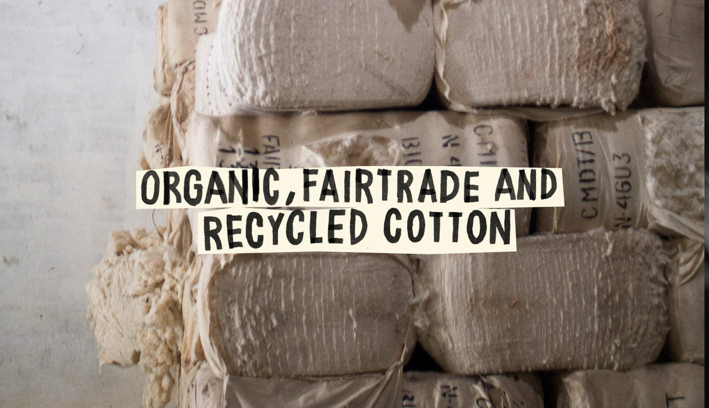 Bales of cotton labeled as organic, fairtrade, and recycled, stacked in a storage area.