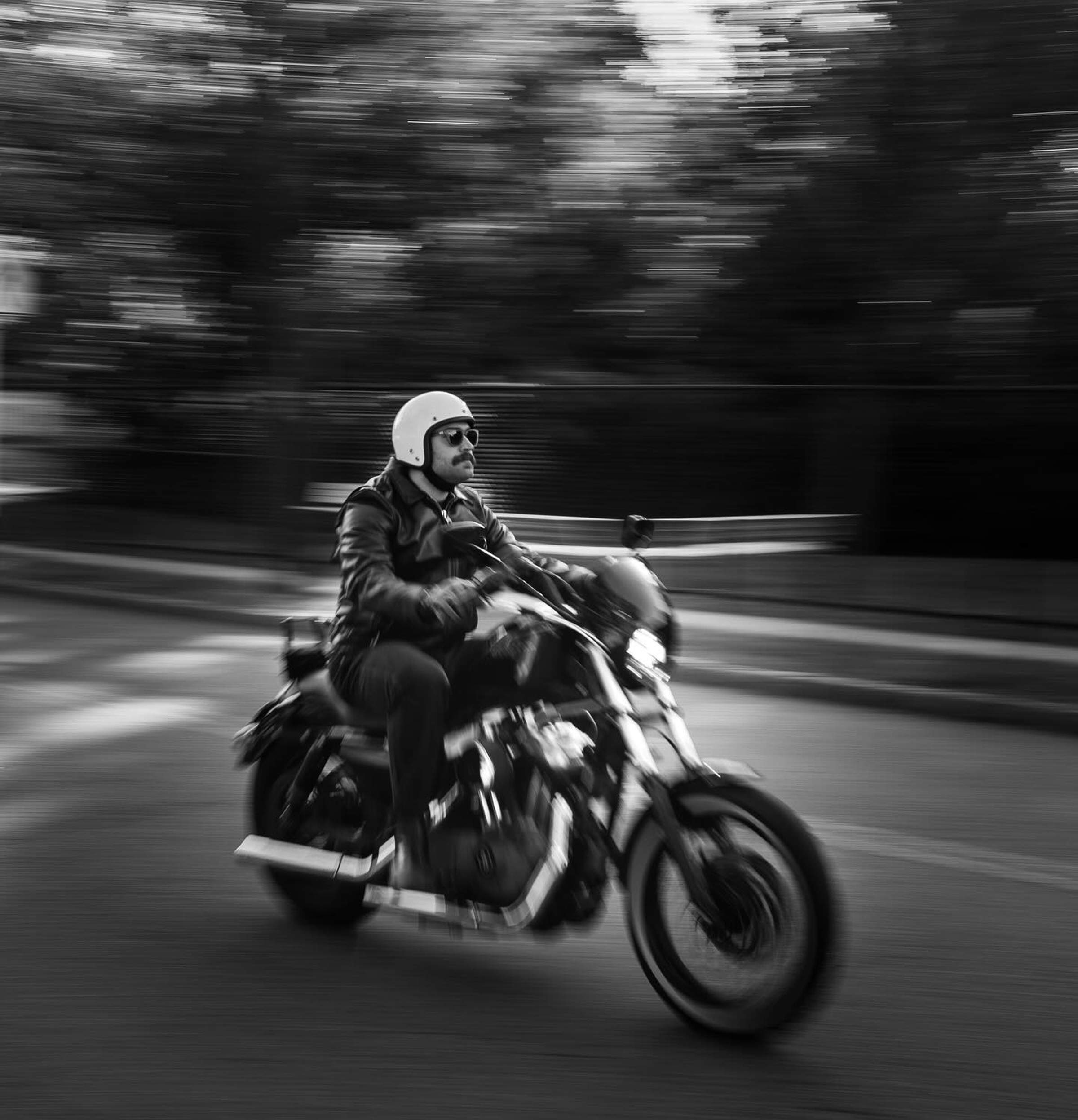 Black and white image of a person in a helmet riding a motorcycle at speed, with a blurred background indicating motion.