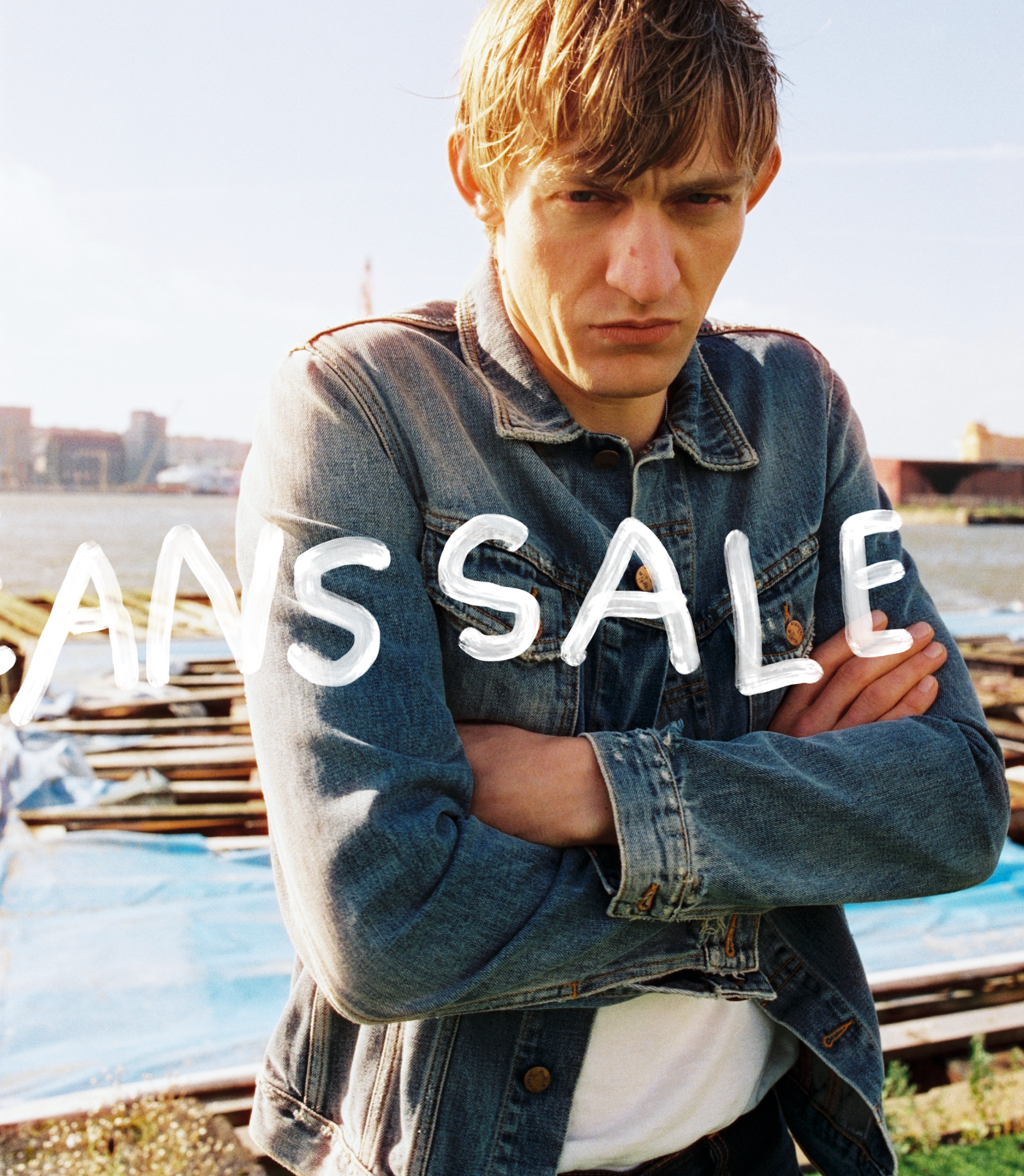 A person in a denim jacket stands with arms crossed by a waterfront, text reading "JANS SALE" is overlaid on the image.