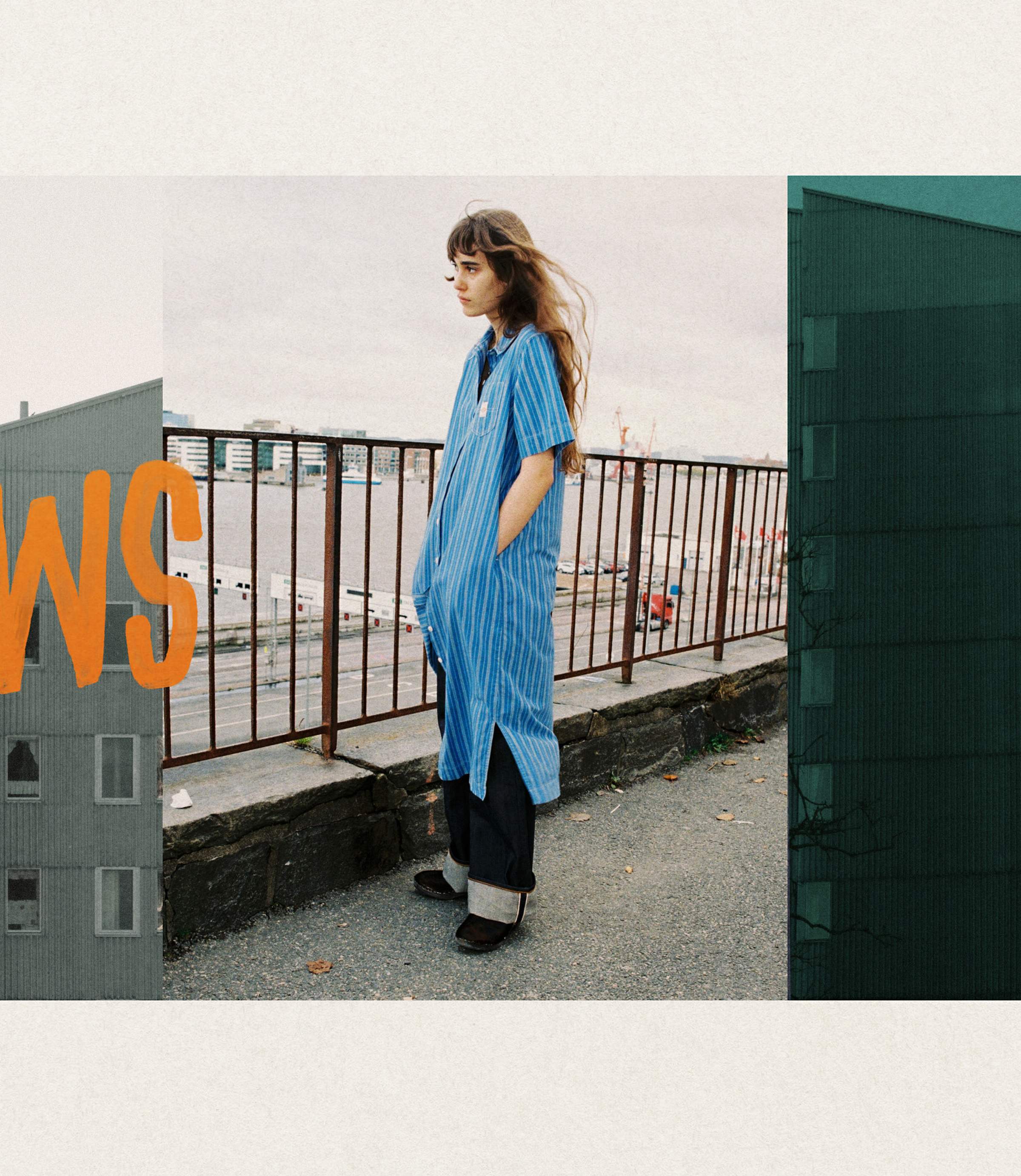 A person with long hair wearing a blue-striped shirt stands near a railing by the water, with buildings and a large "WS" graphic on the sides.