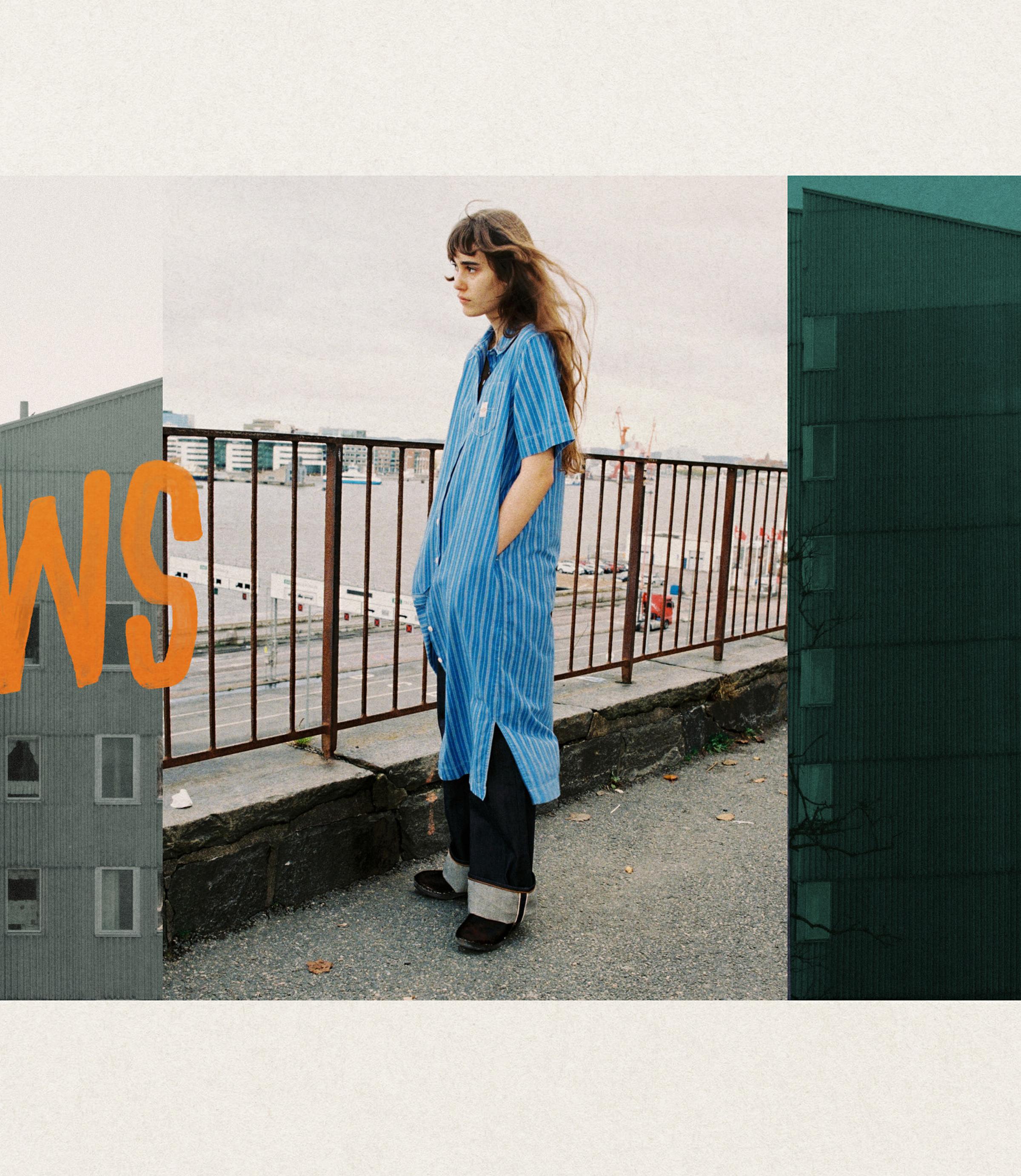 A person with long hair wearing a blue-striped shirt stands near a railing by the water, with buildings and a large "WS" graphic on the sides.