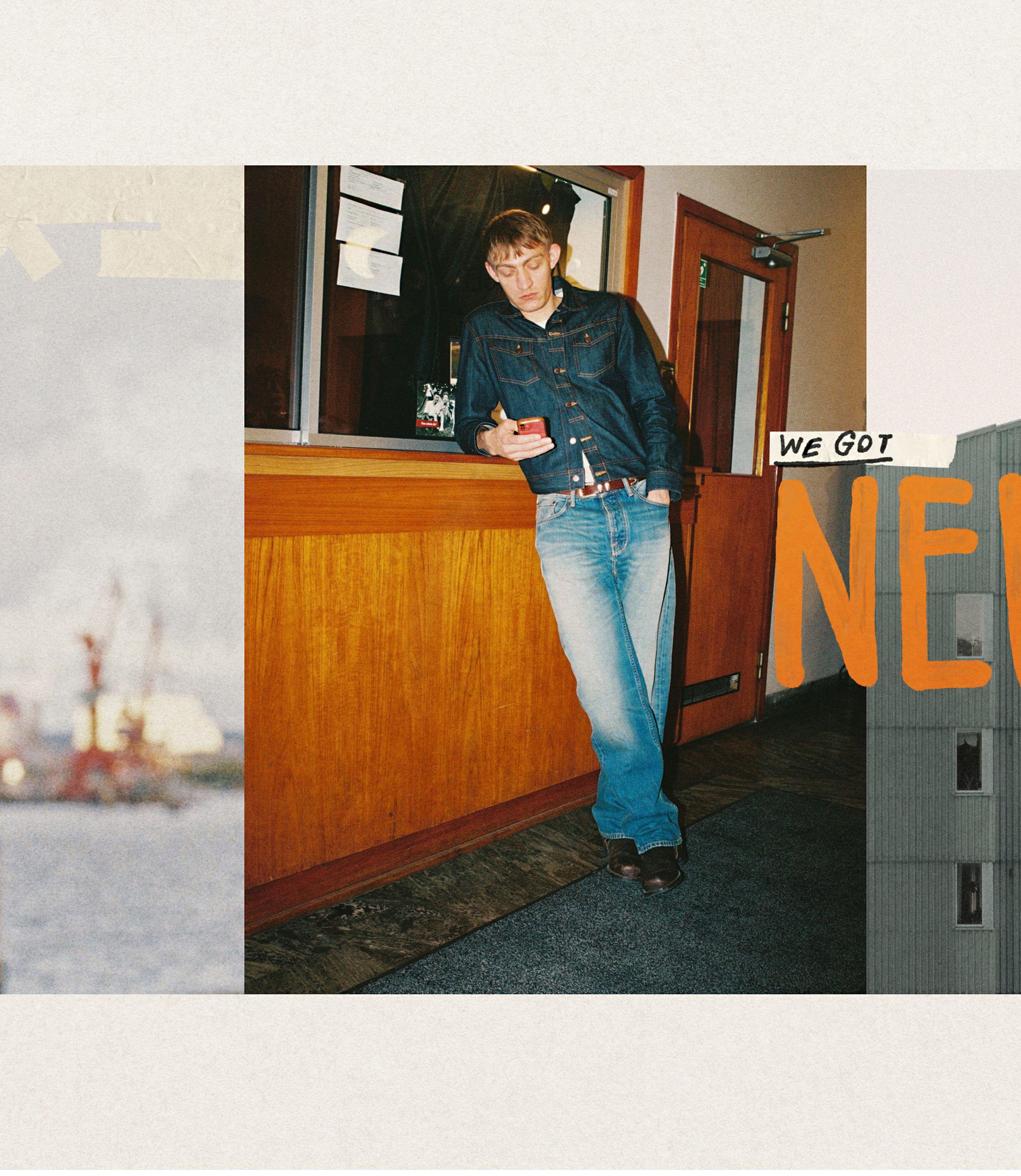 A person in a denim jacket and jeans leans on a wooden counter, looking at their phone. The text "We Got New" is partially visible.