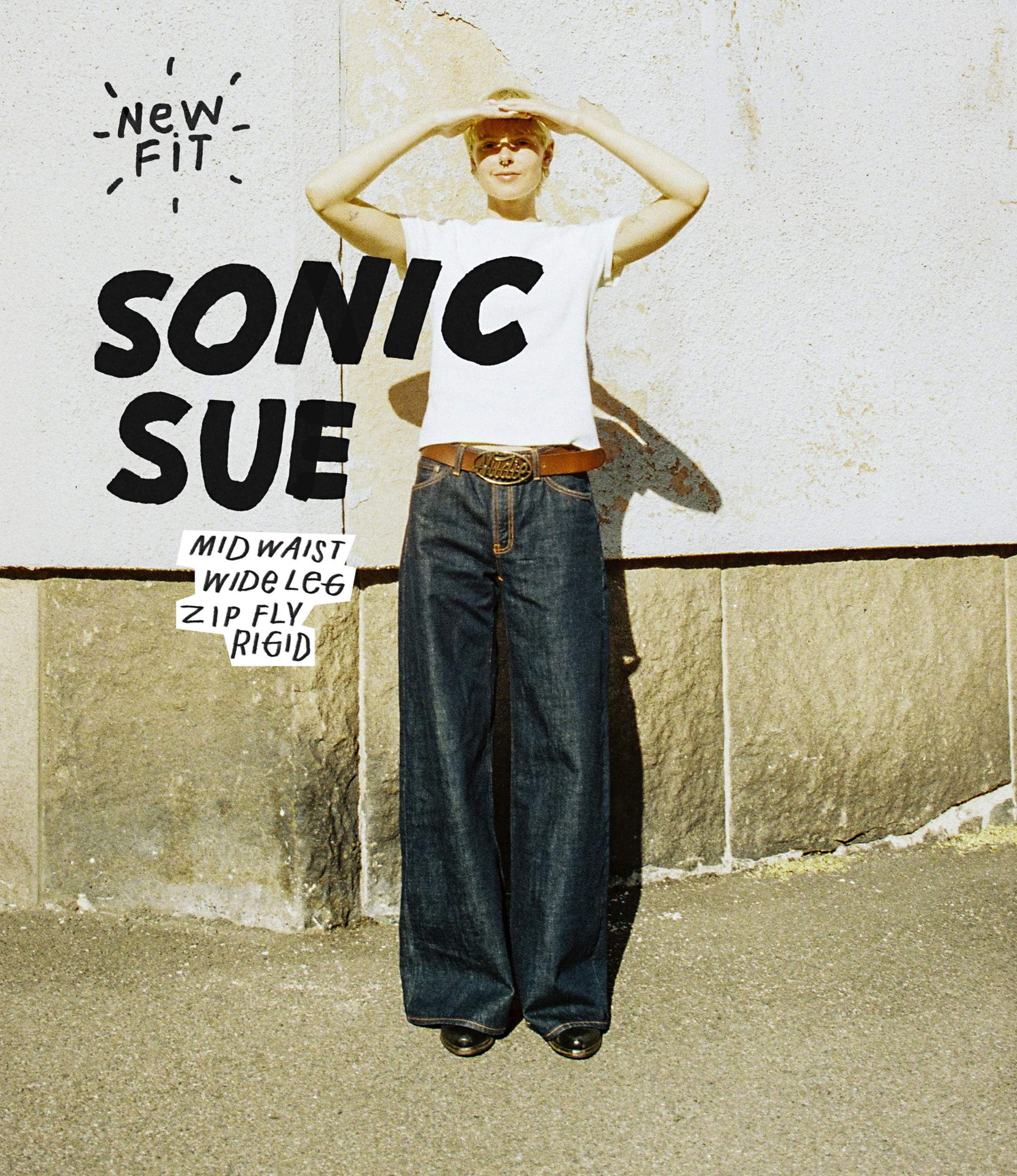 Person wearing a white shirt and wide-leg jeans, shielding eyes from the sun, with text about the jeans' features on the left.