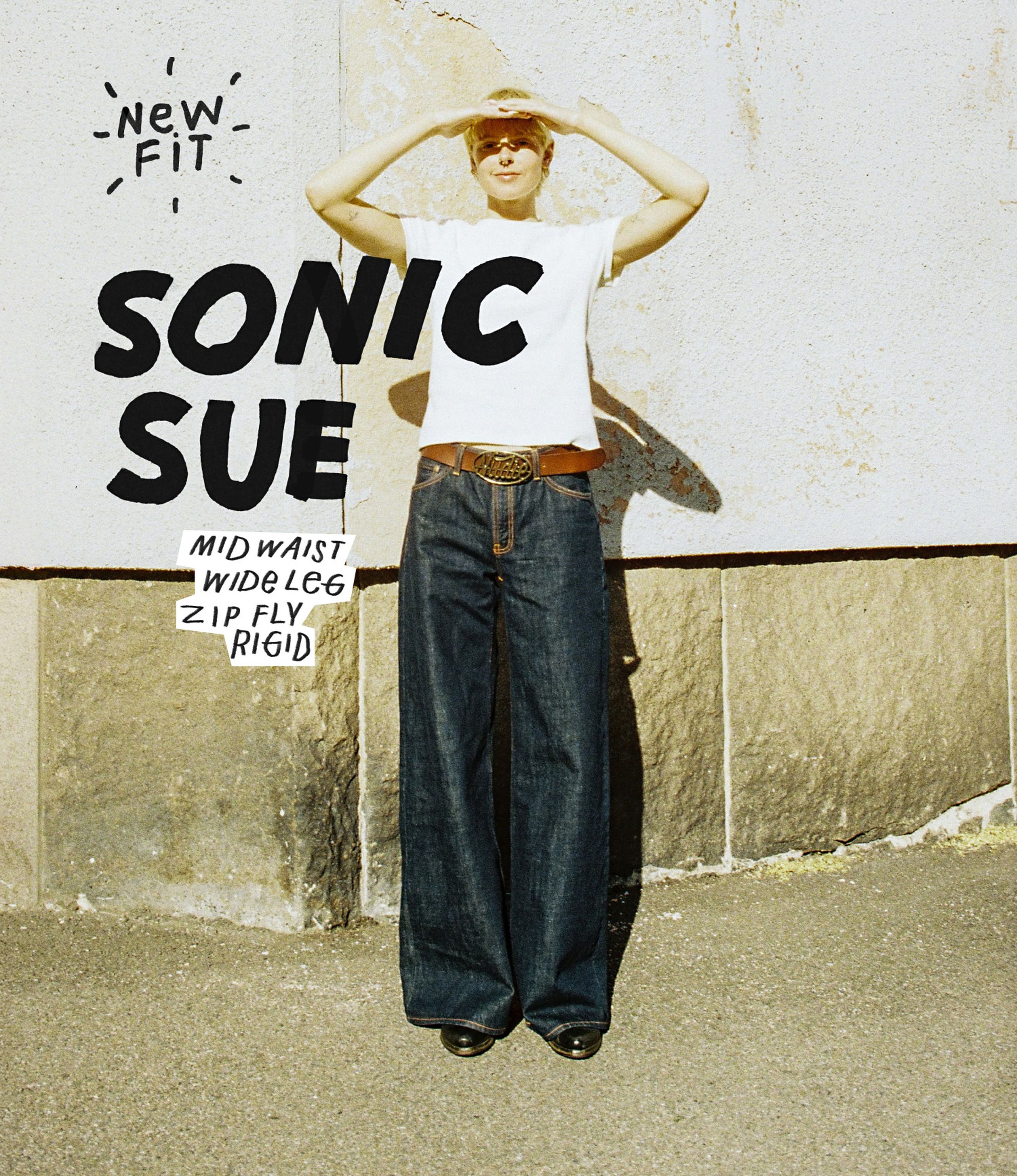 Person wearing a white shirt and wide-leg jeans, shielding eyes from the sun, with text about the jeans' features on the left.