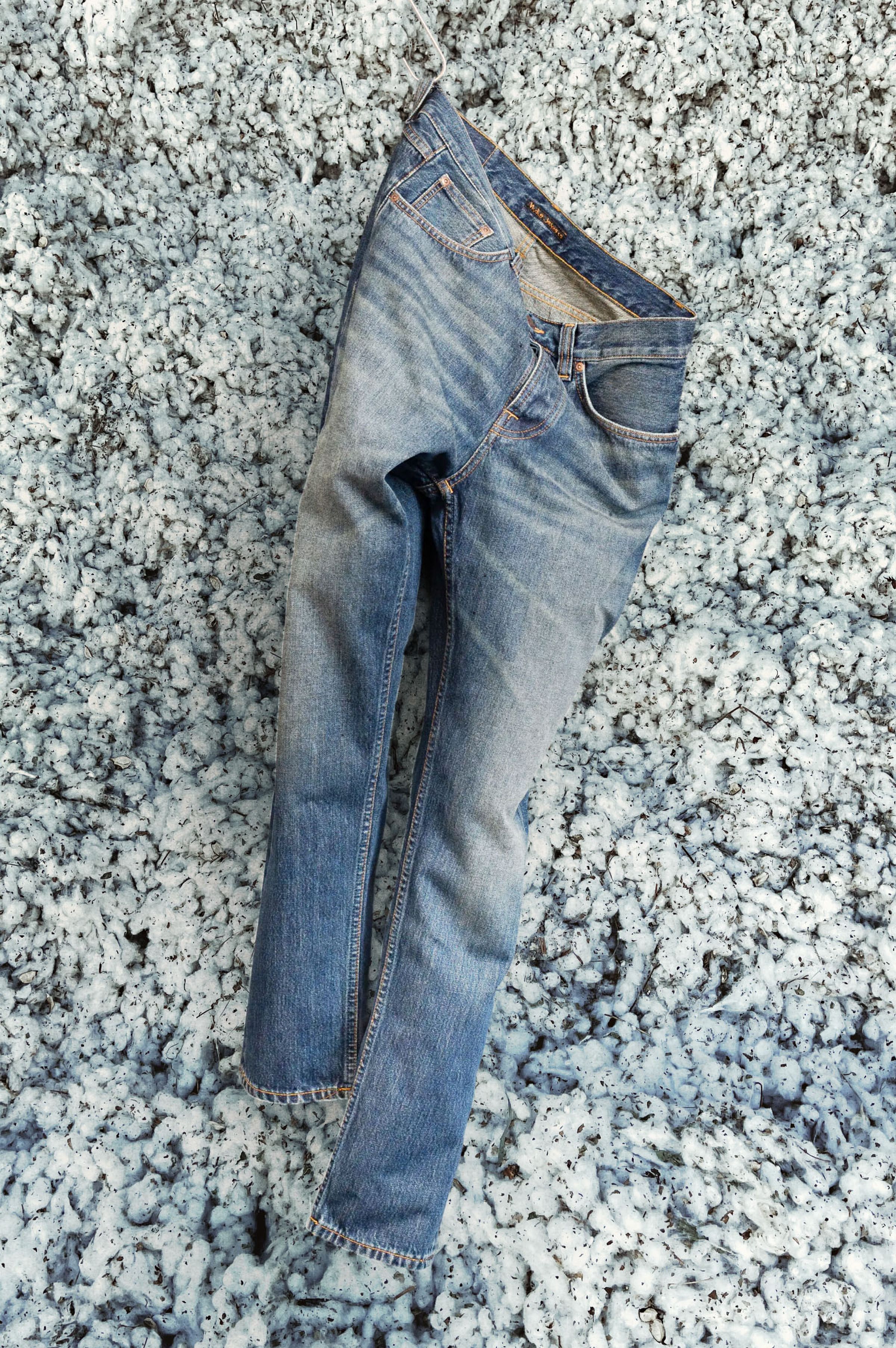 Blue Nudie Jeans hangs on a backdrop with regenerative organic cotton.