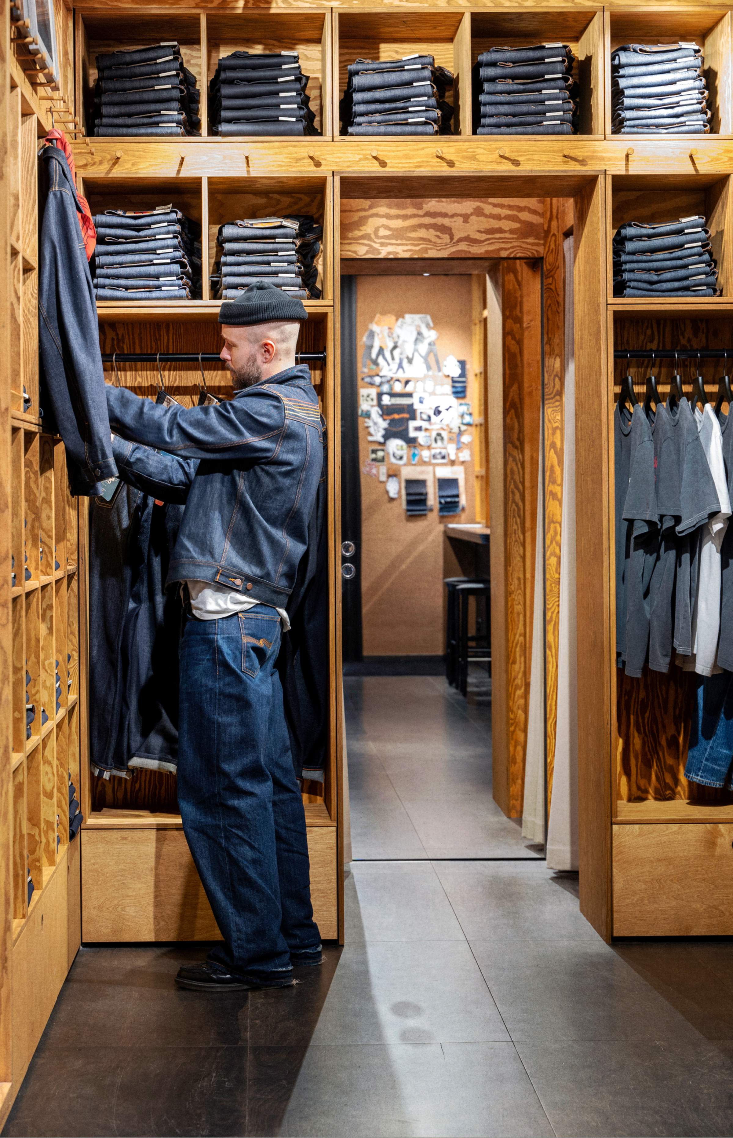A person browses denim jackets in a store with wooden shelves filled with neatly folded jeans and shirts.