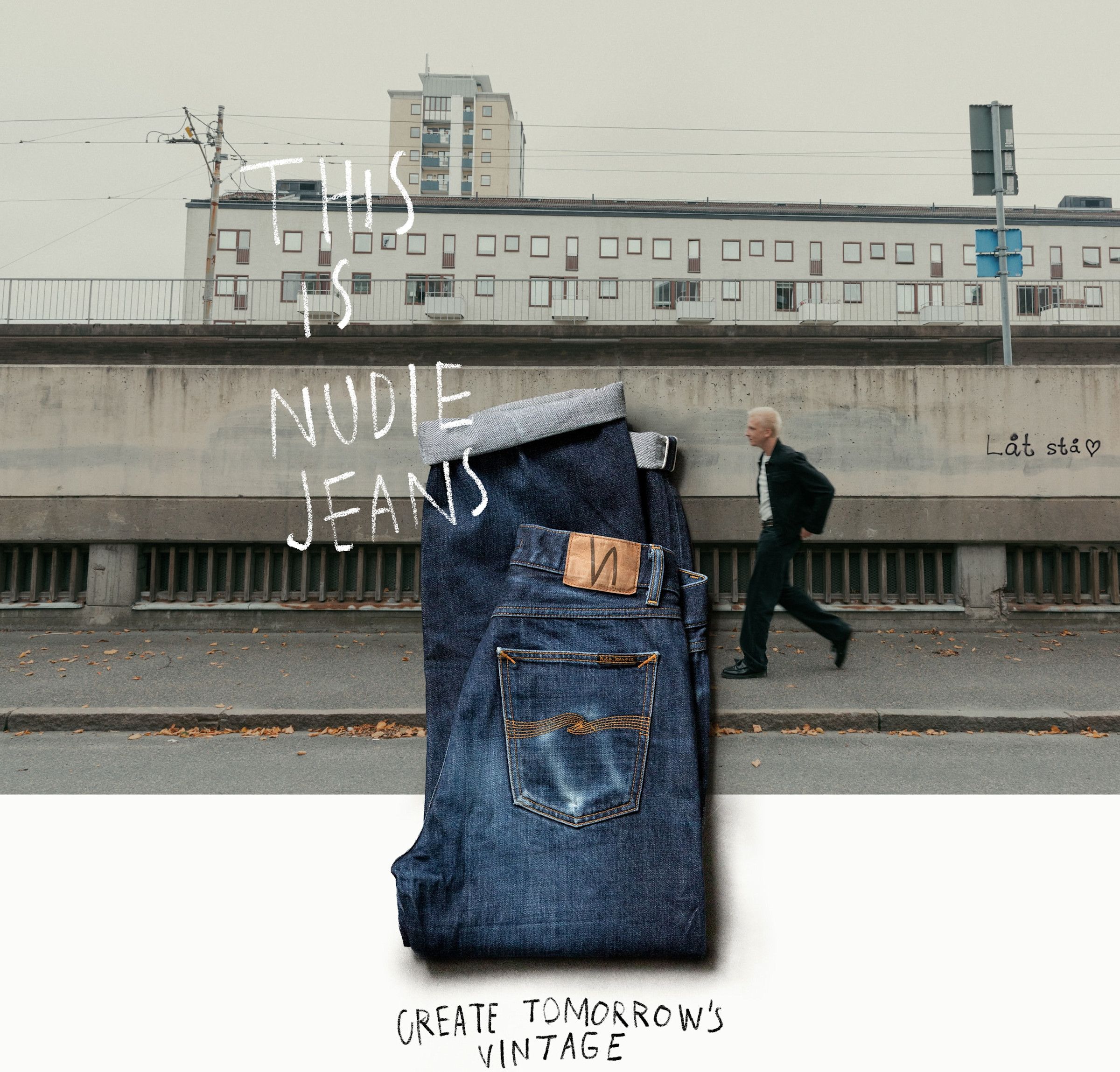 Folded blue jeans on a street background with a walking man. Text reads, "This is Nudie Jeans. Create Tomorrow's Vintage."